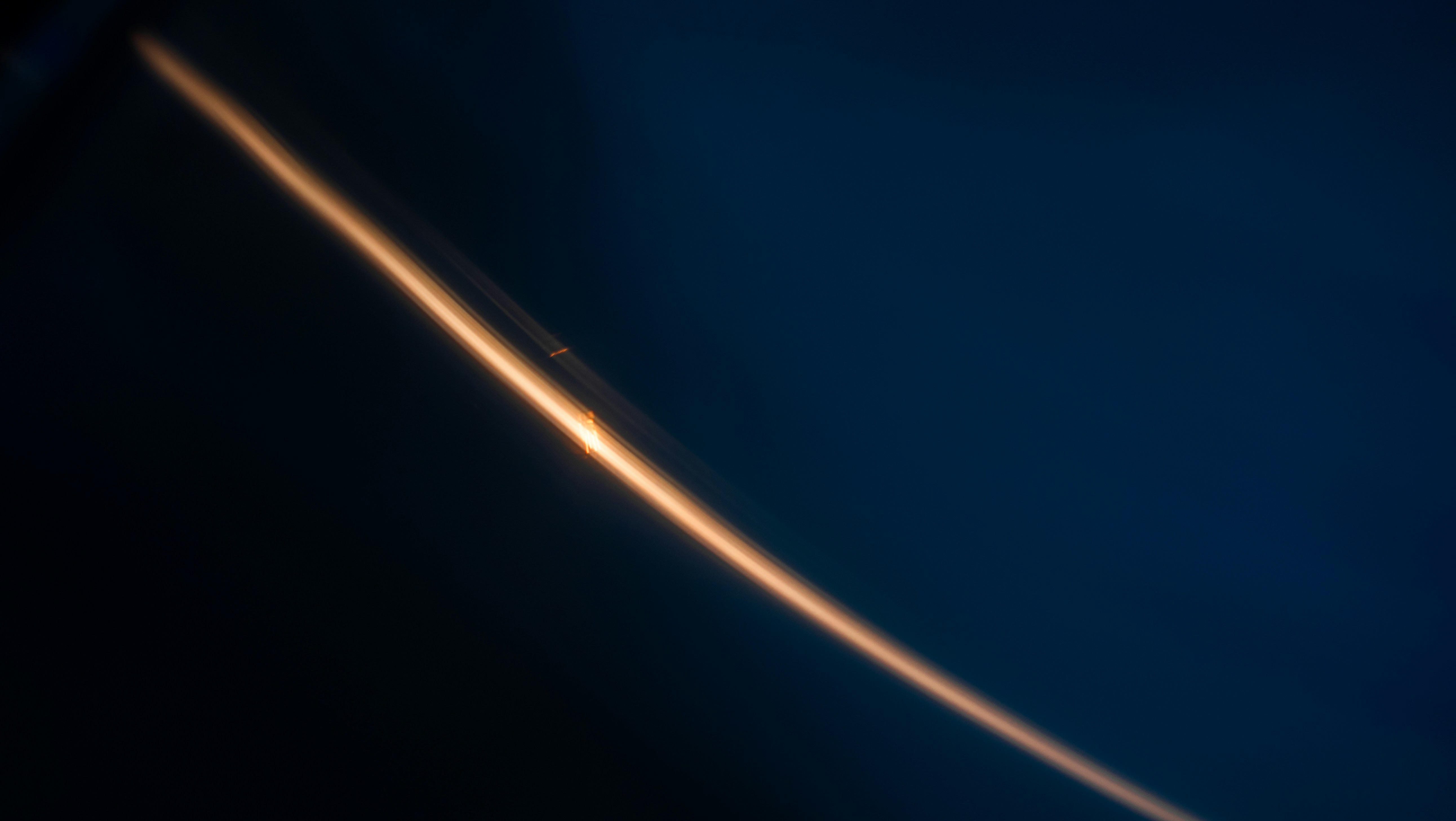 A single curved streak of warm orange light against a dark blue background