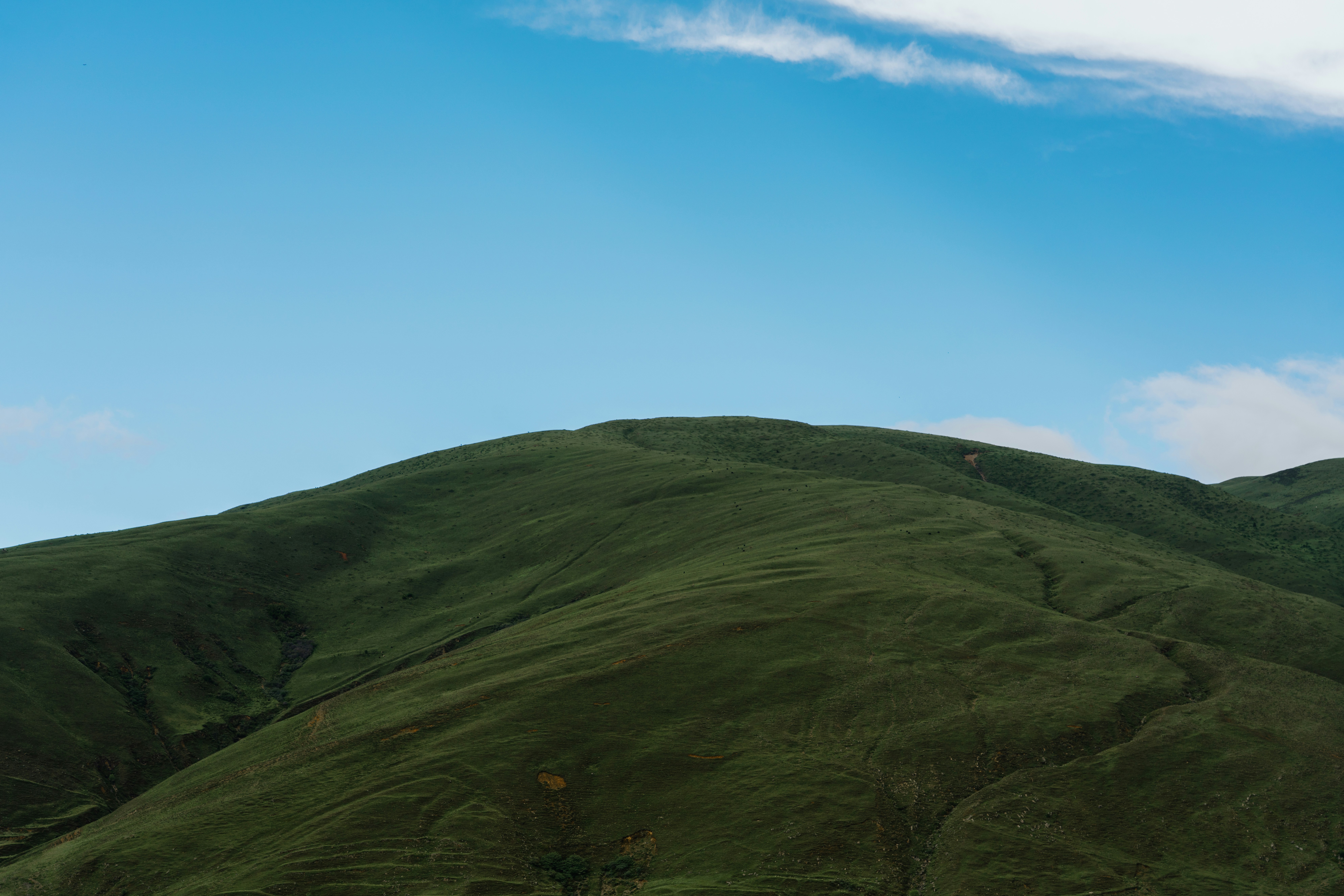 A green mountain slope under a clear blue sky with light clouds