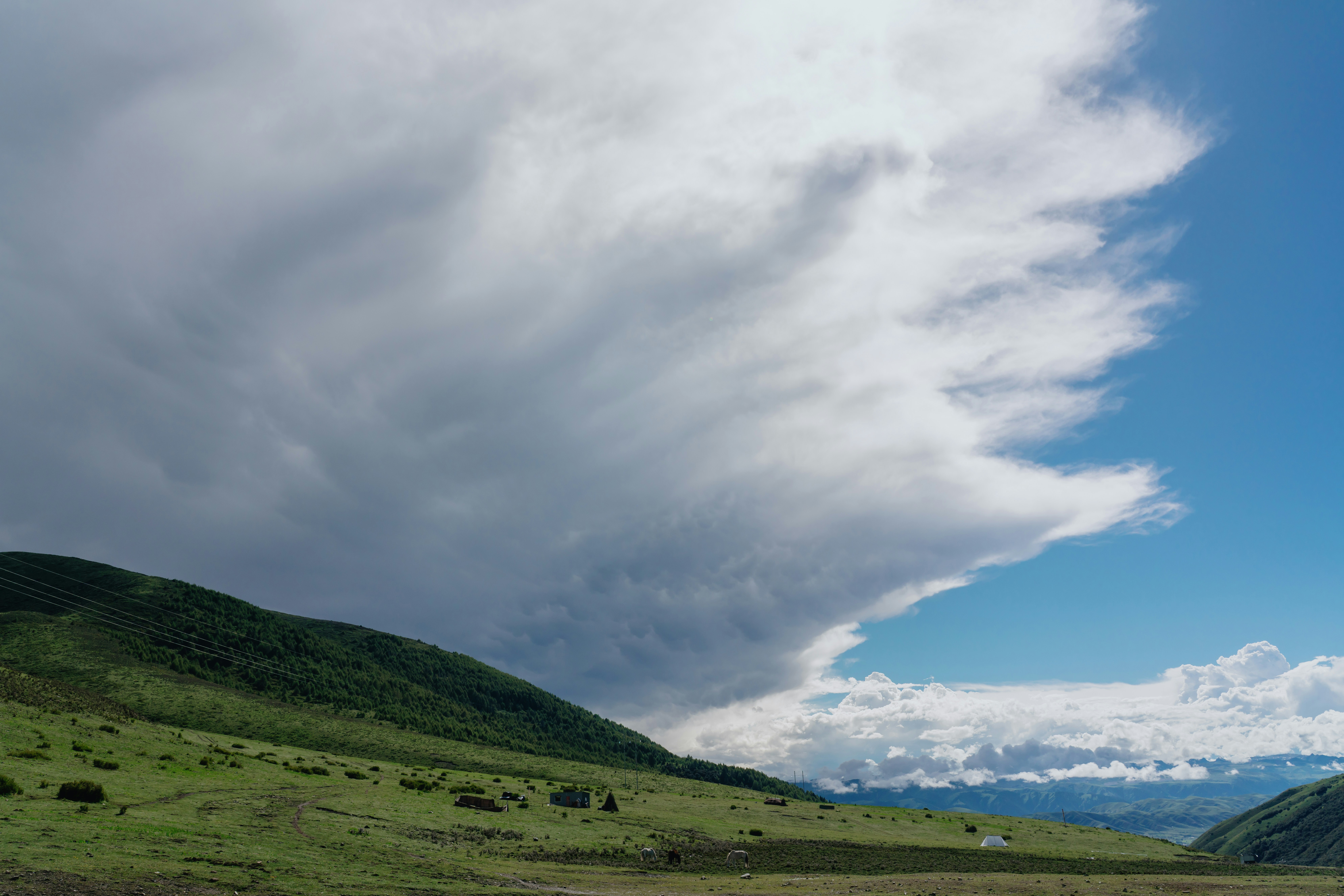 A large dark storm cloud over a green mountain slope with scattered small structures