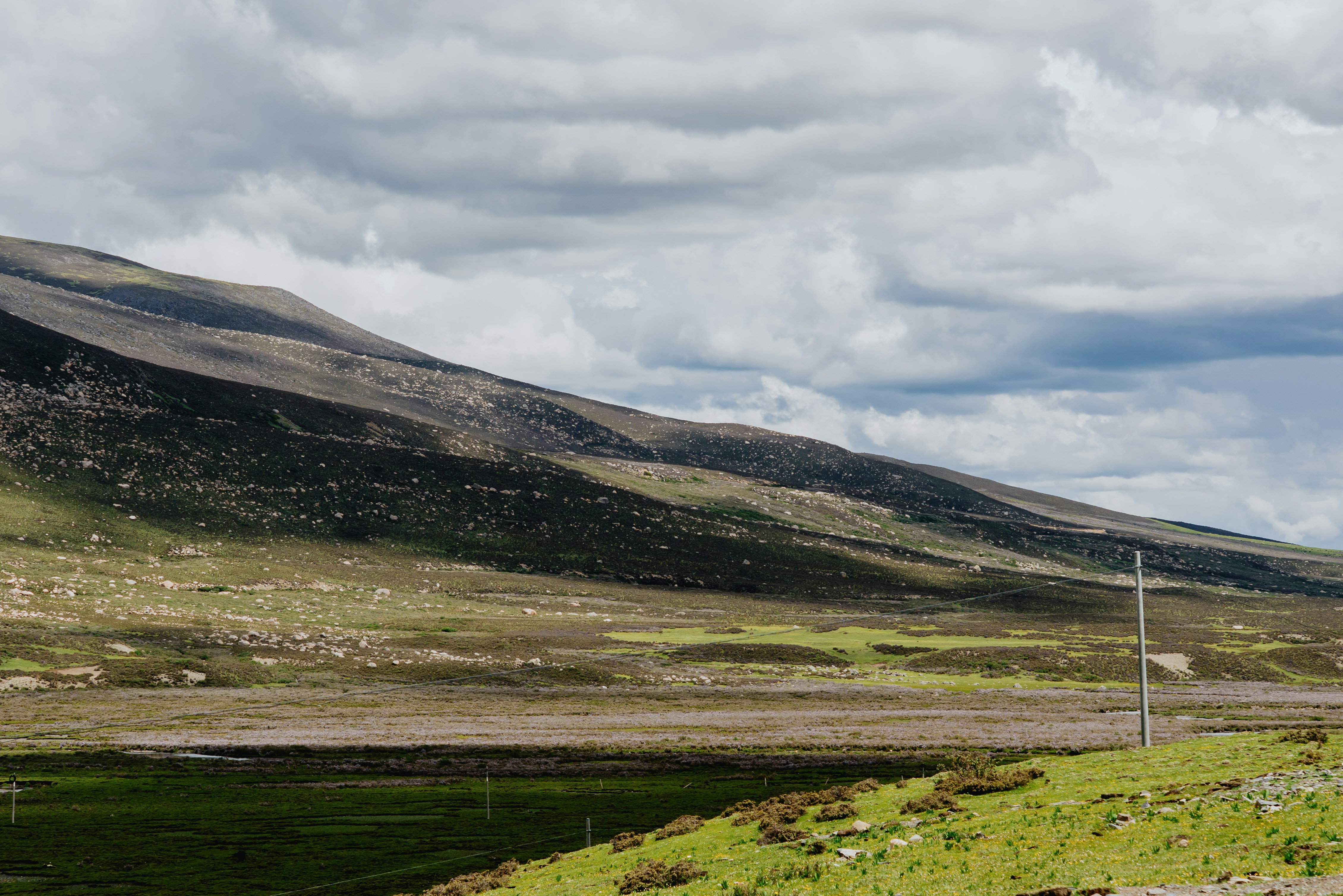 A vast green valley beneath a dark mountain slope under a cloudy sky