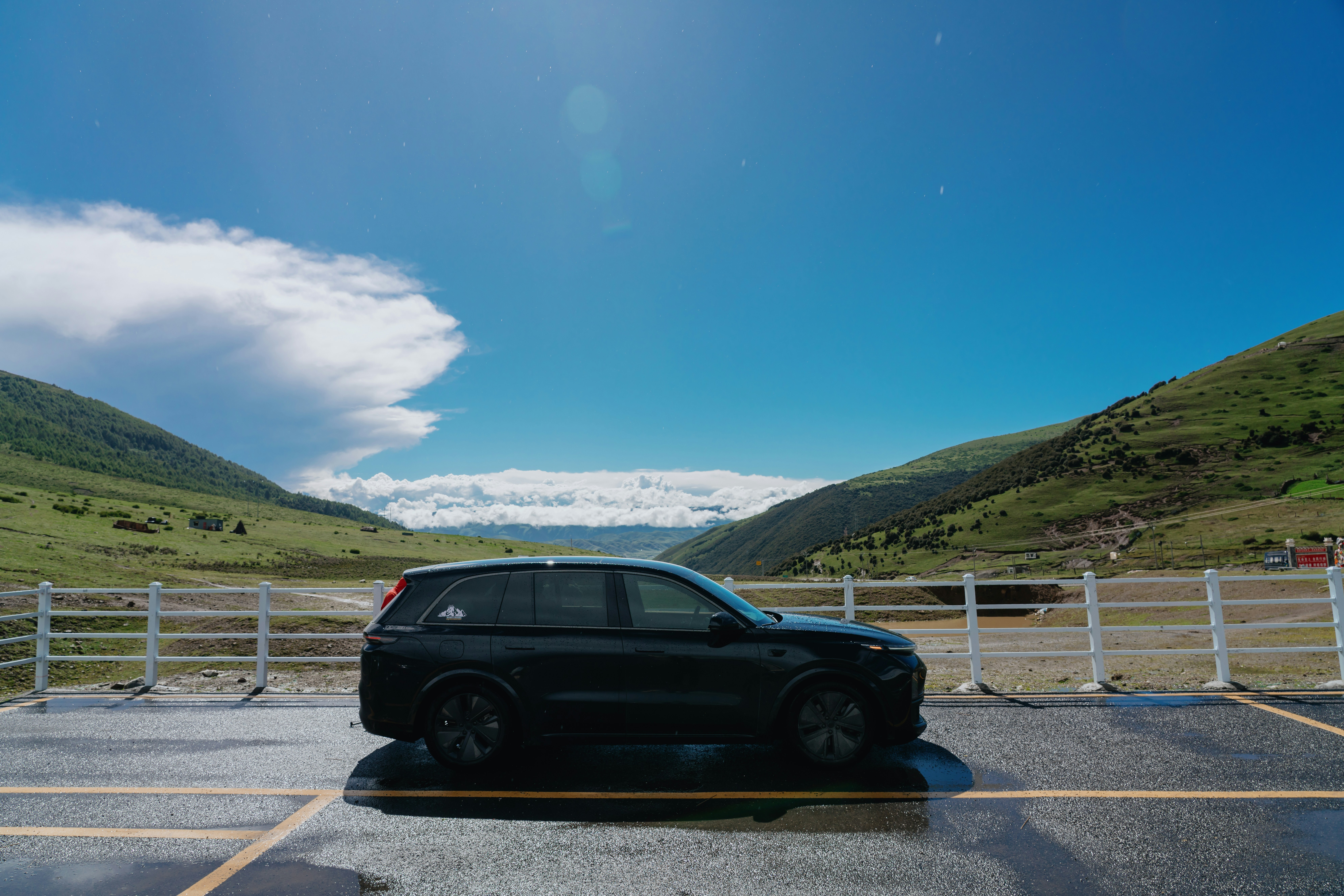 A black SUV parked on an asphalt road beside a white fence in mountains