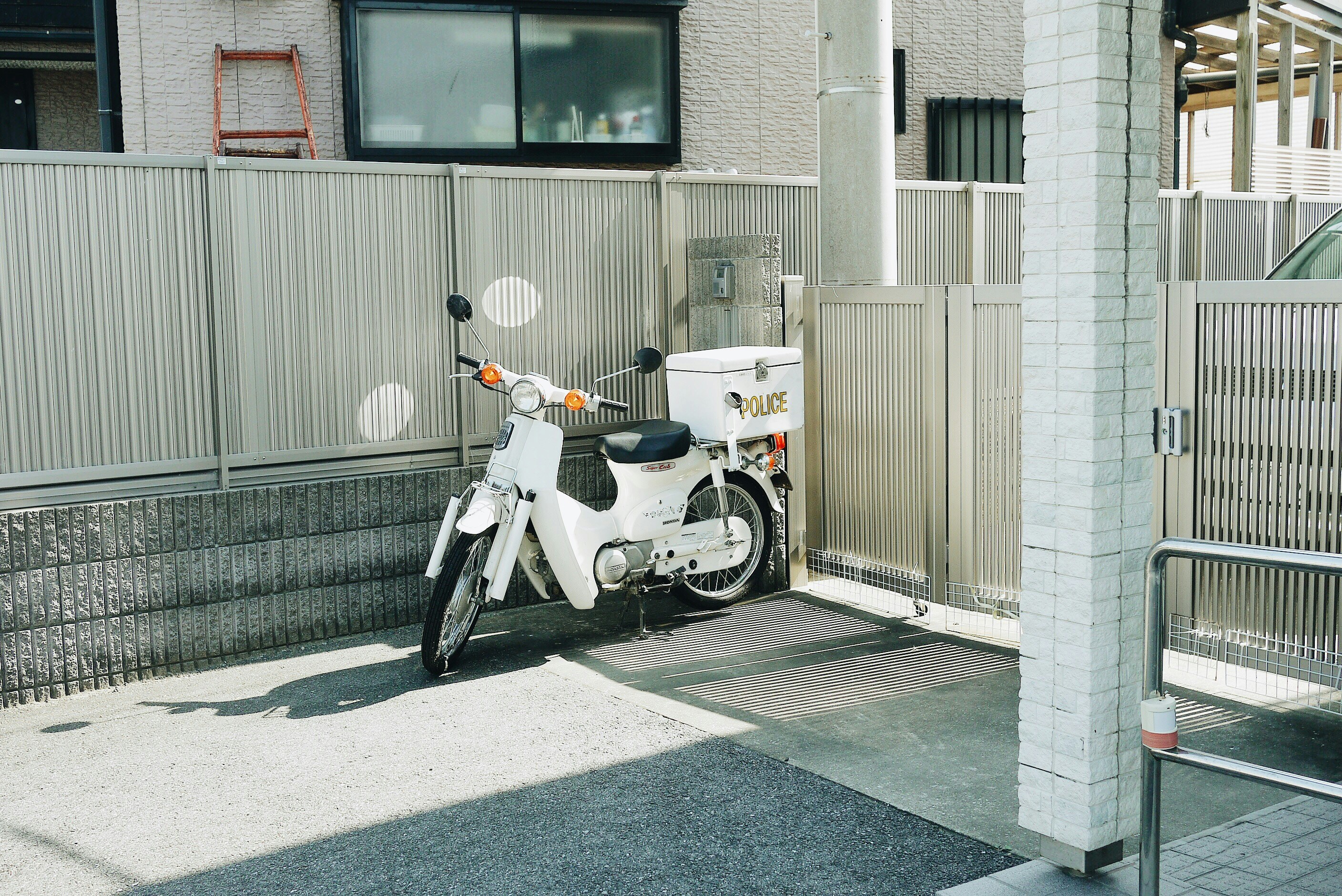 A white motorcycle with a police storage box parked by a metal fence