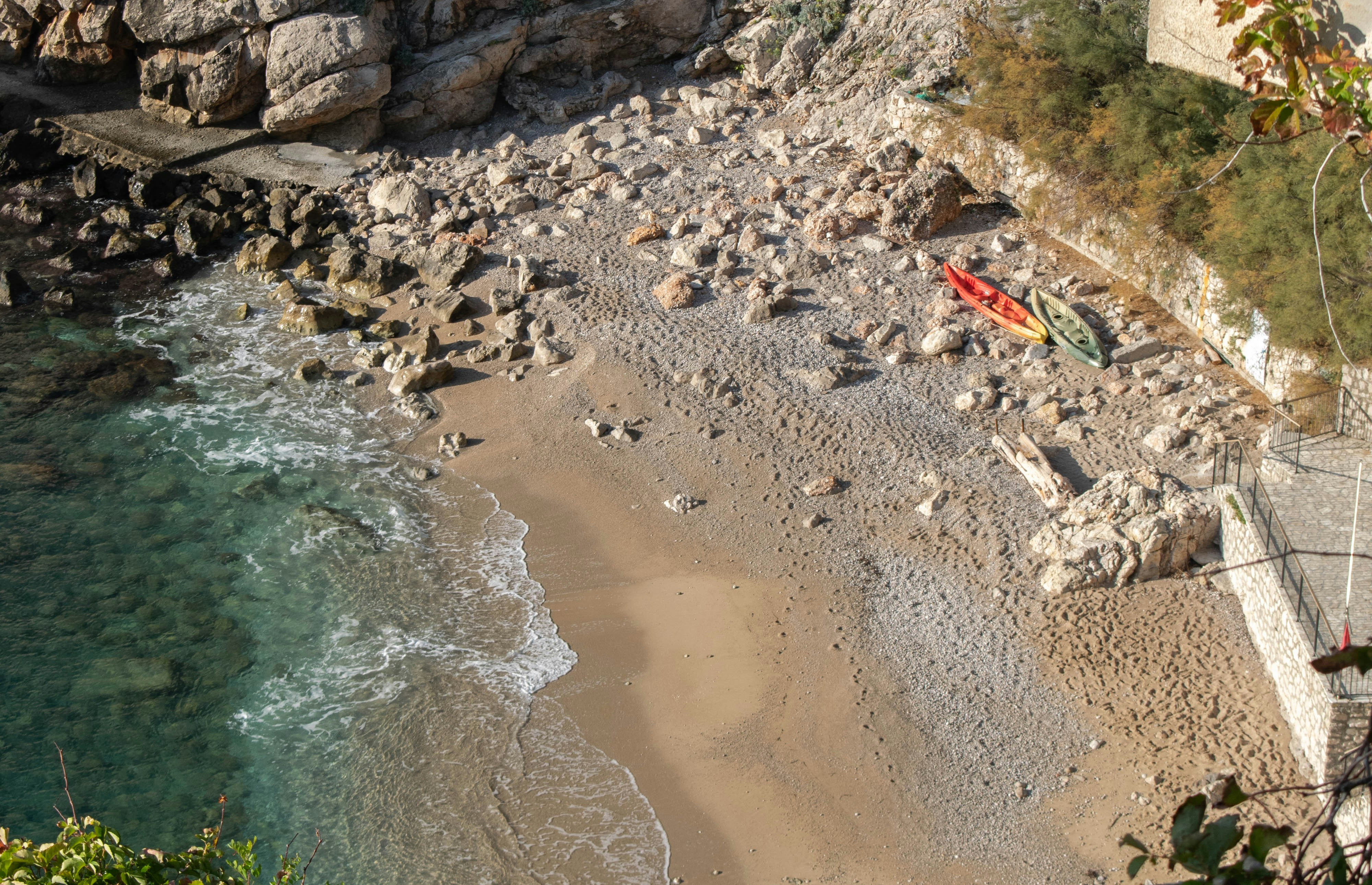 Two kayaks on a rocky beach beside clear turquoise water and cliffs
