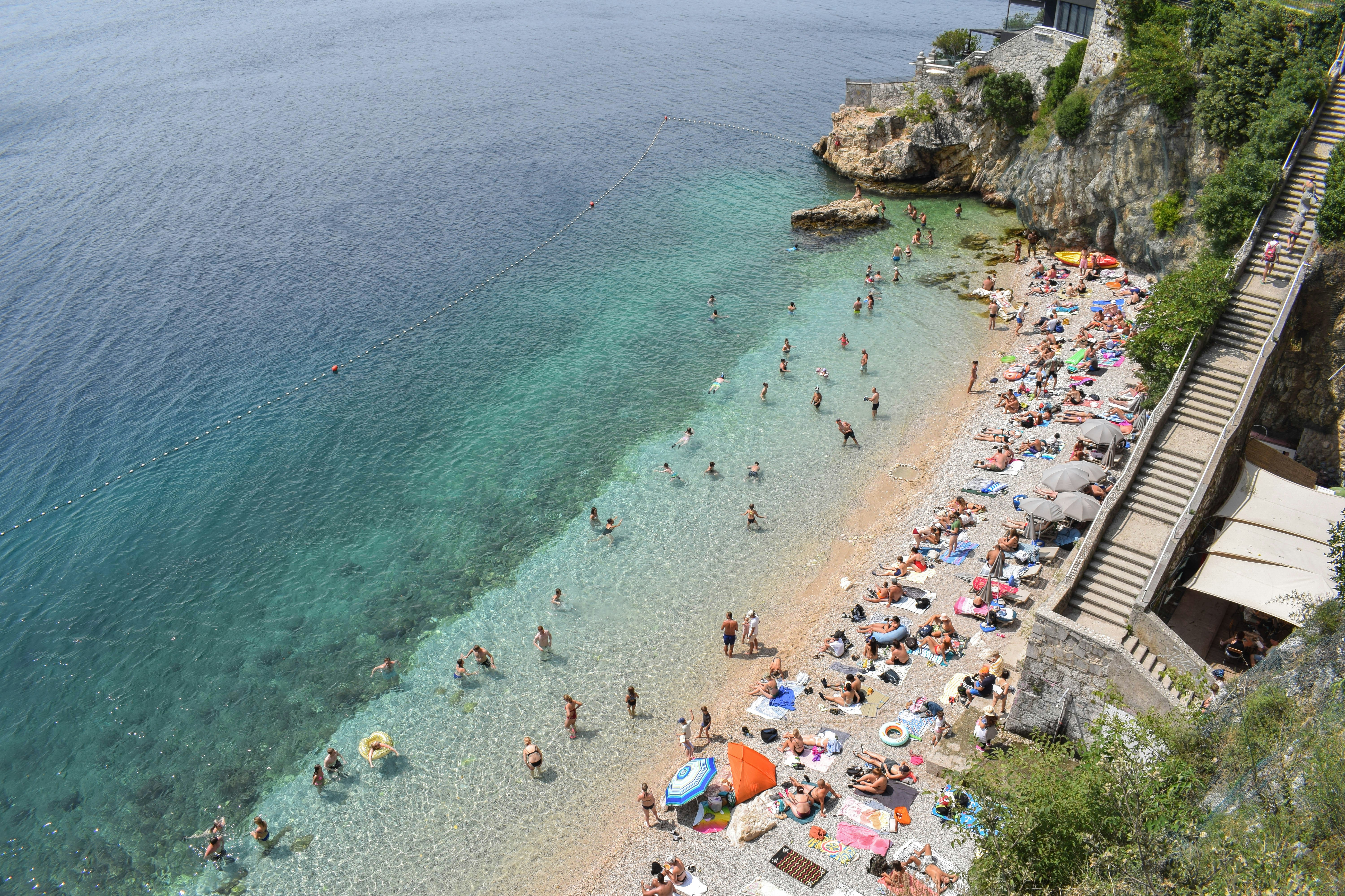 People swimming in clear turquoise water and relaxing on a pebble beach