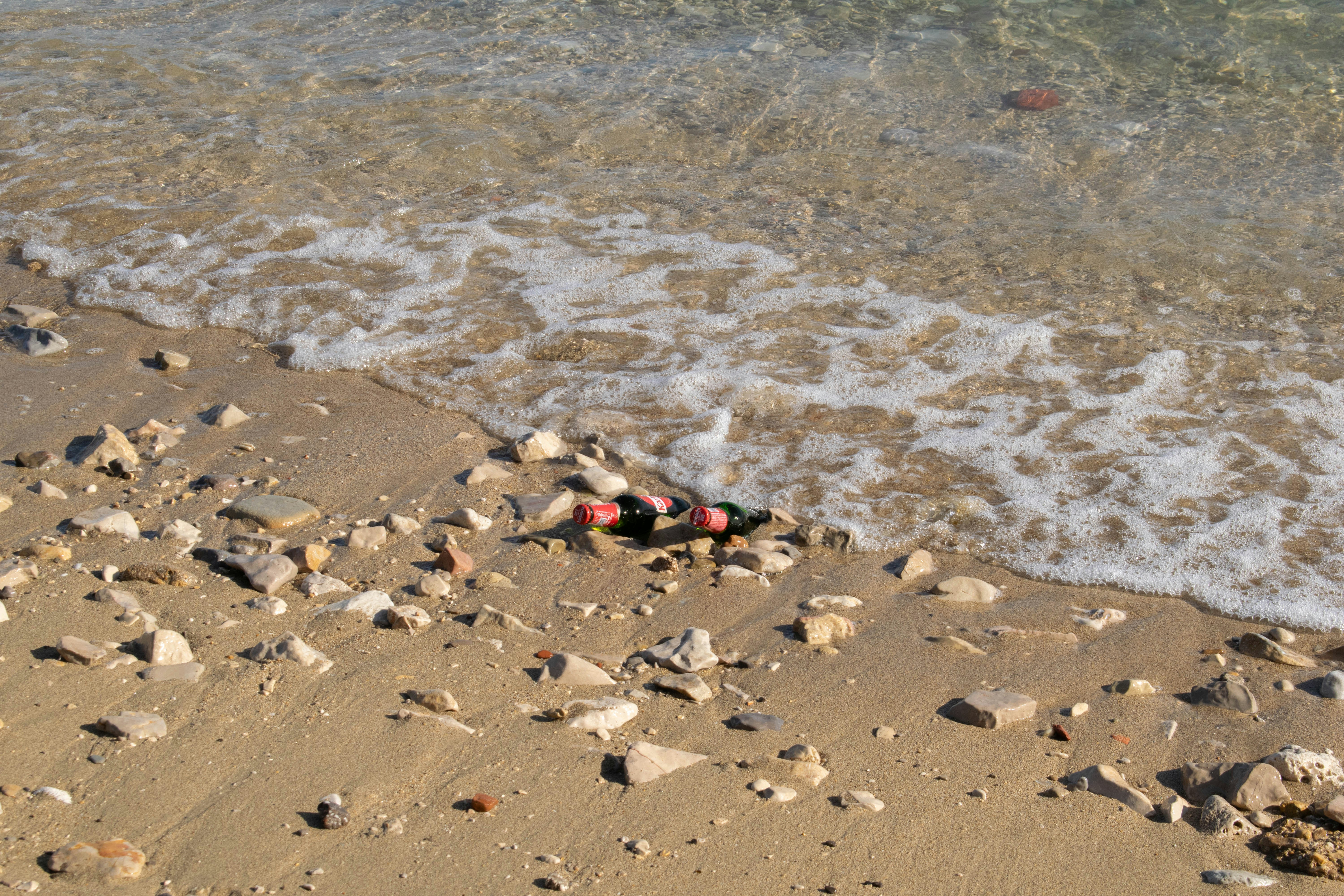 Two glass bottles on a rocky sandy beach with gentle waves washing ashore