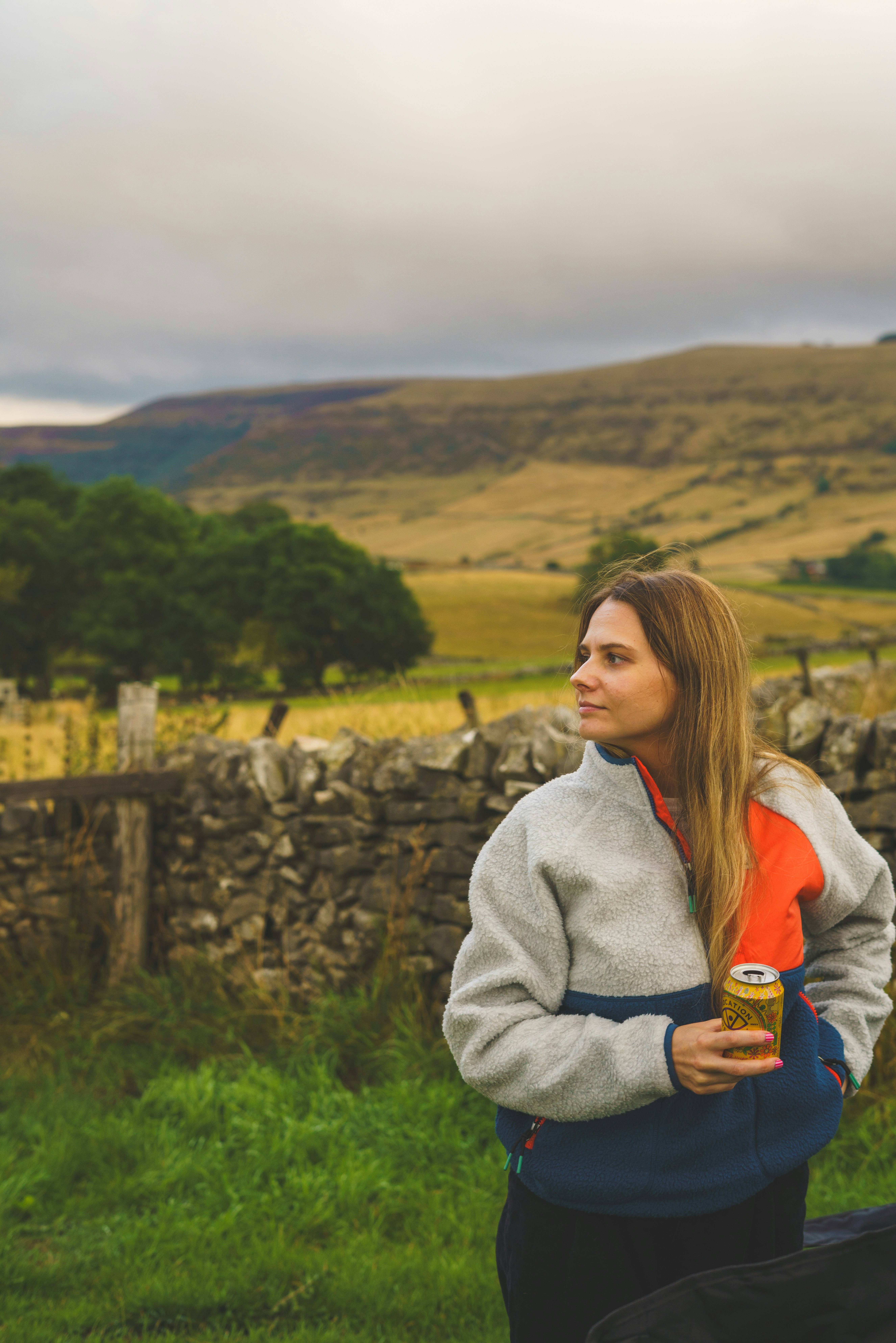 A woman in a fleece jacket holding a can by a stone wall