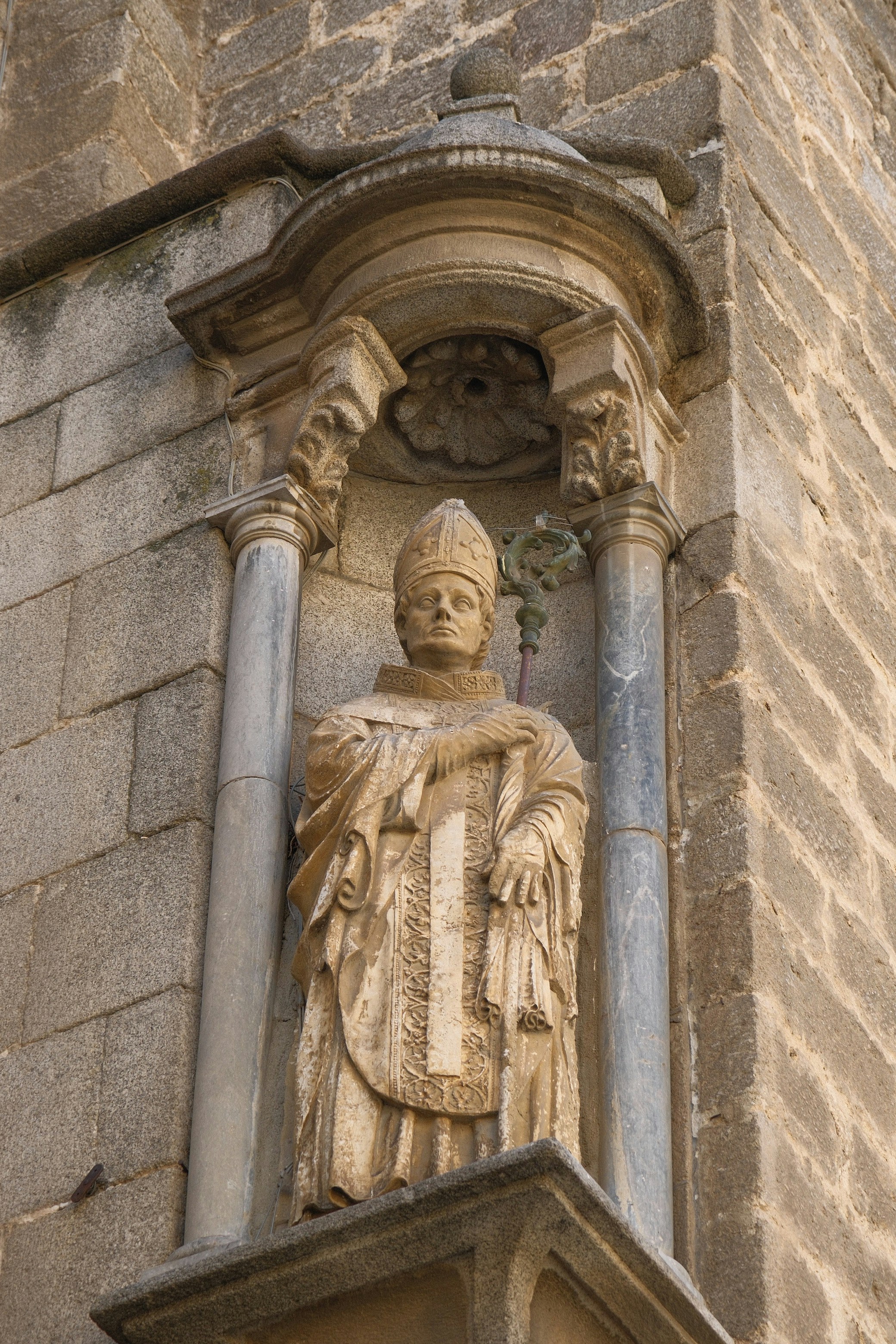 A stone statue of a bishop holding a crozier in a wall niche