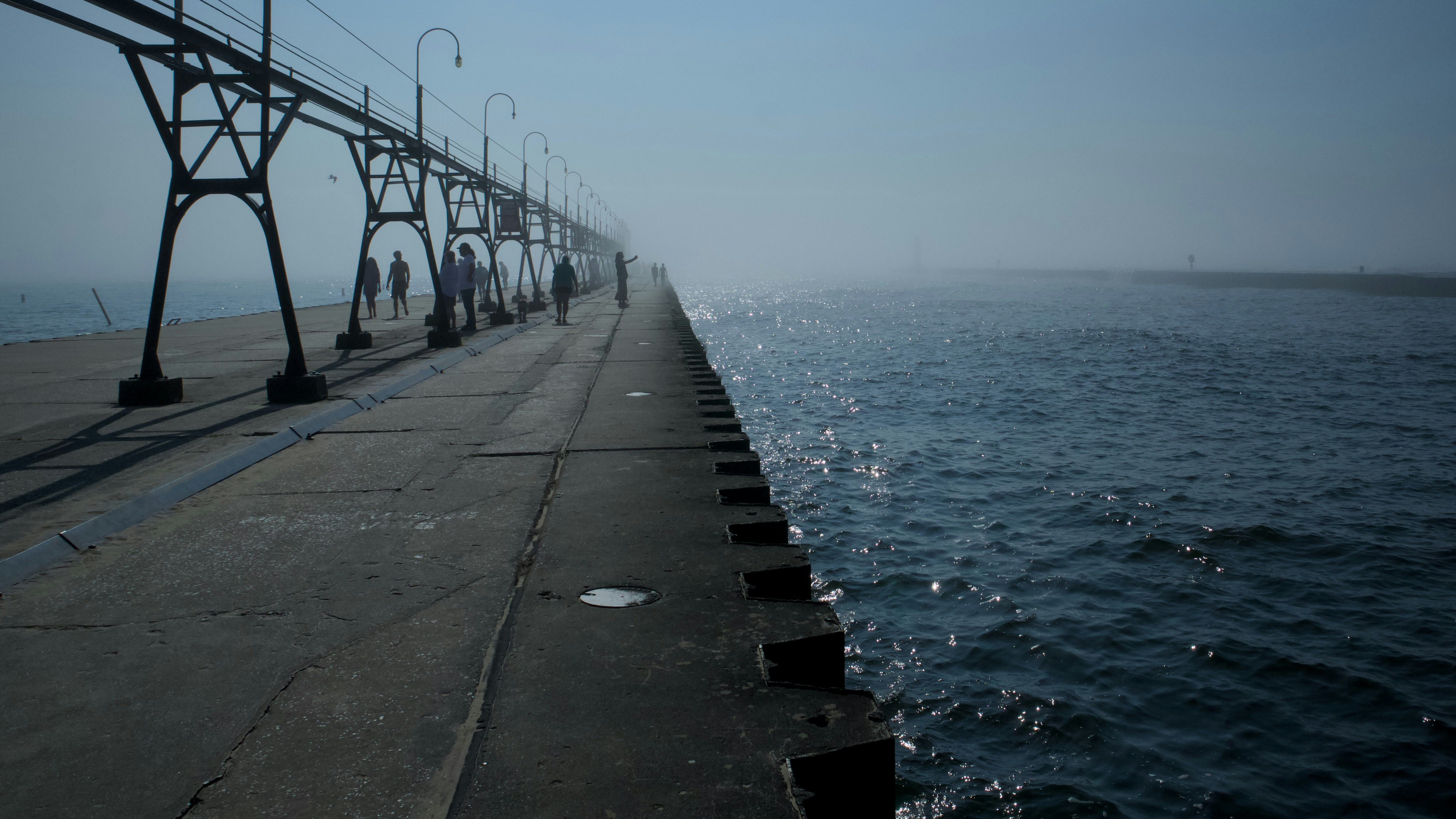 People walking along a concrete pier with a metal catwalk in thick fog