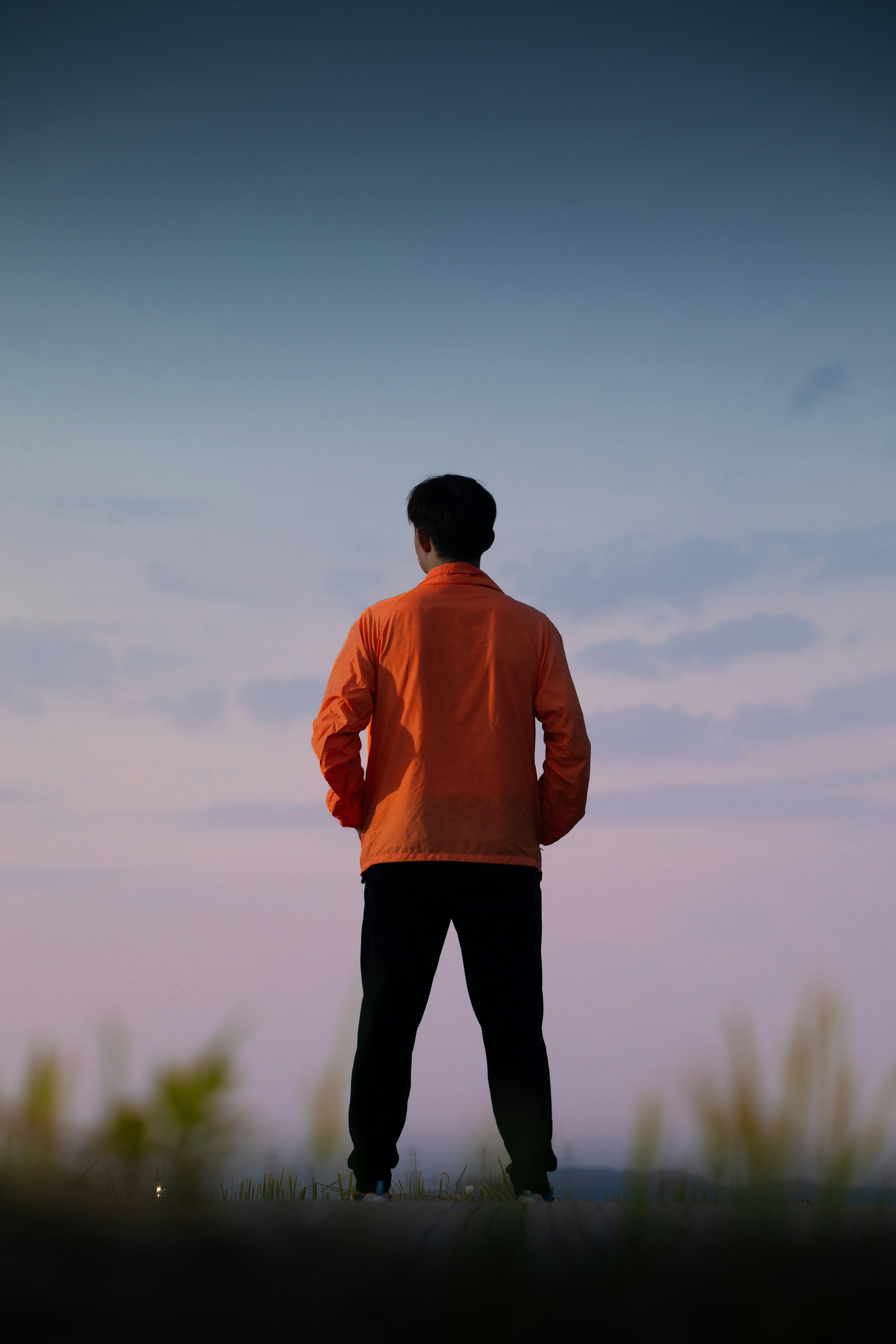 A person in an orange jacket against a soft blue and pink sky