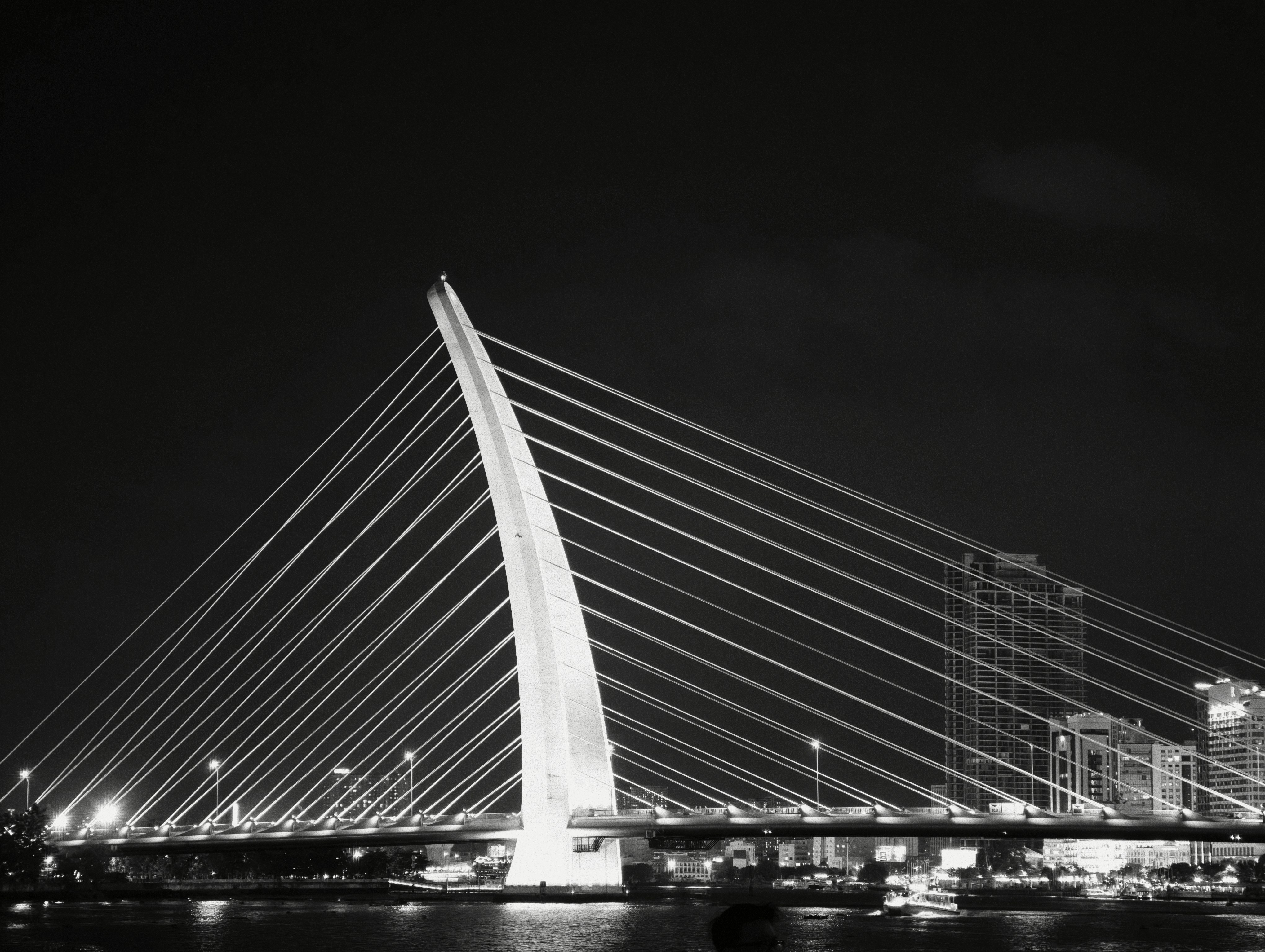 A cable-stayed bridge with a single pylon illuminated at night over a river