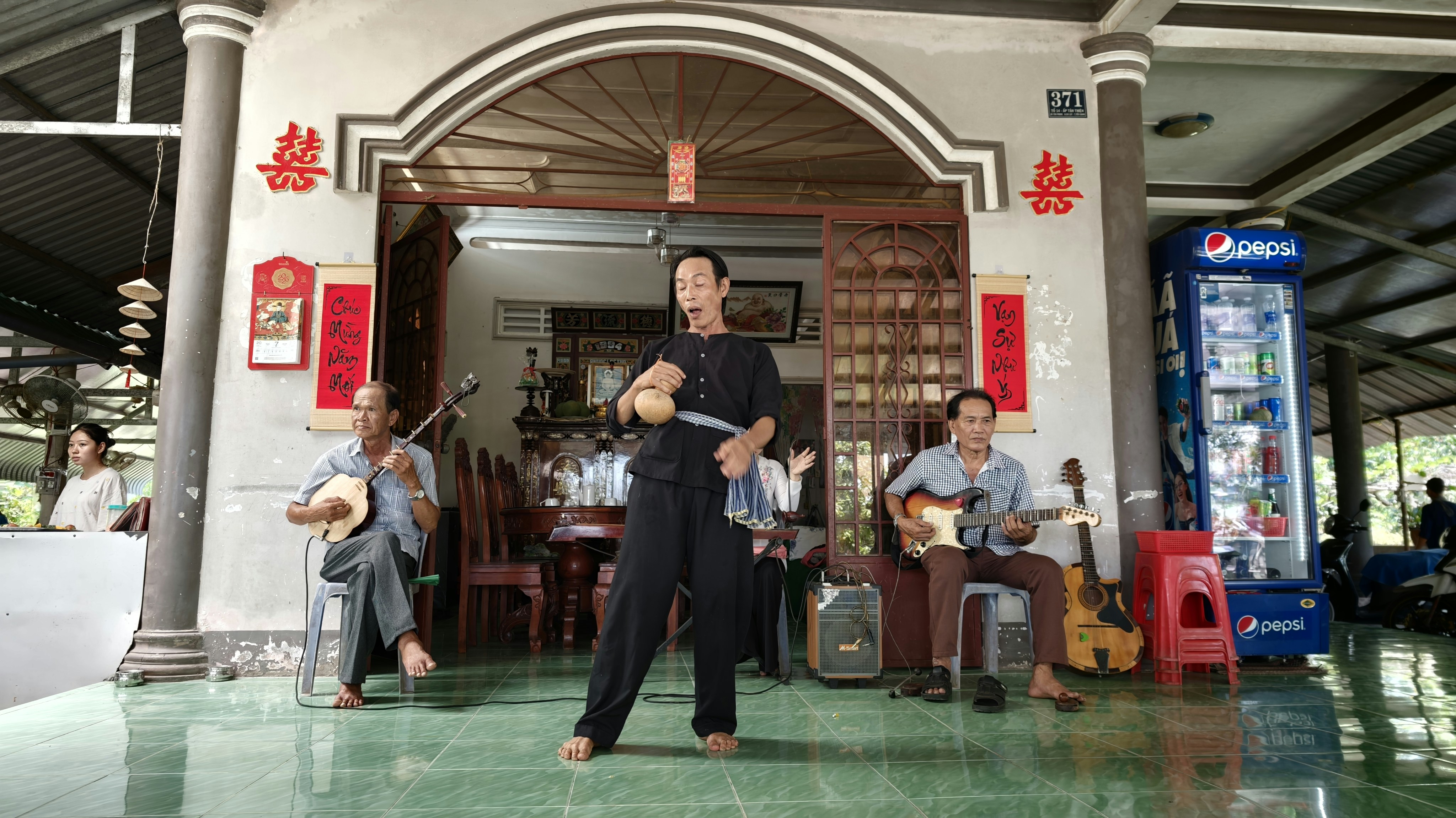 Three men performing music on a tiled porch in front of a house