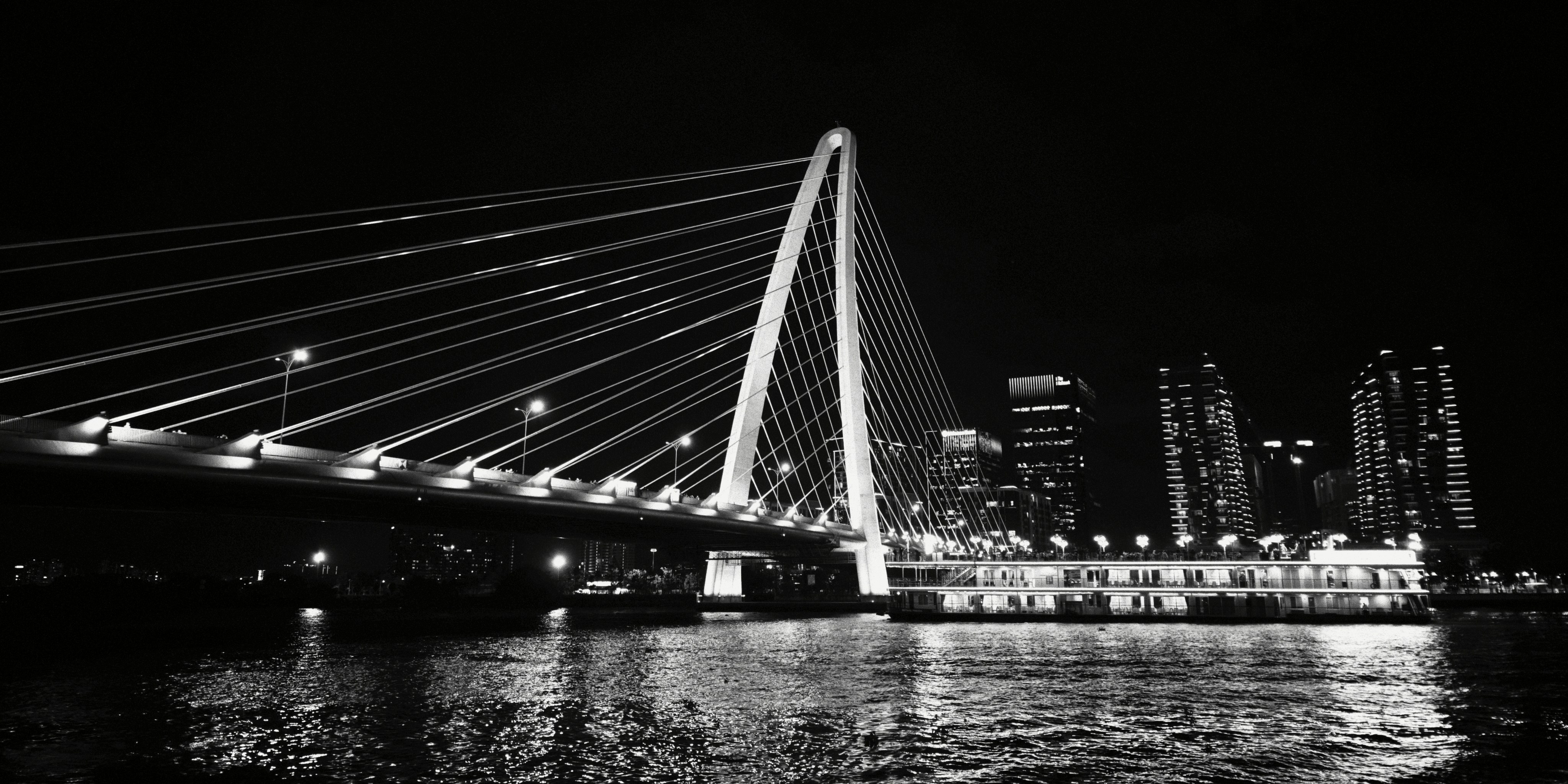A cable-stayed bridge illuminated at night over a river with city buildings