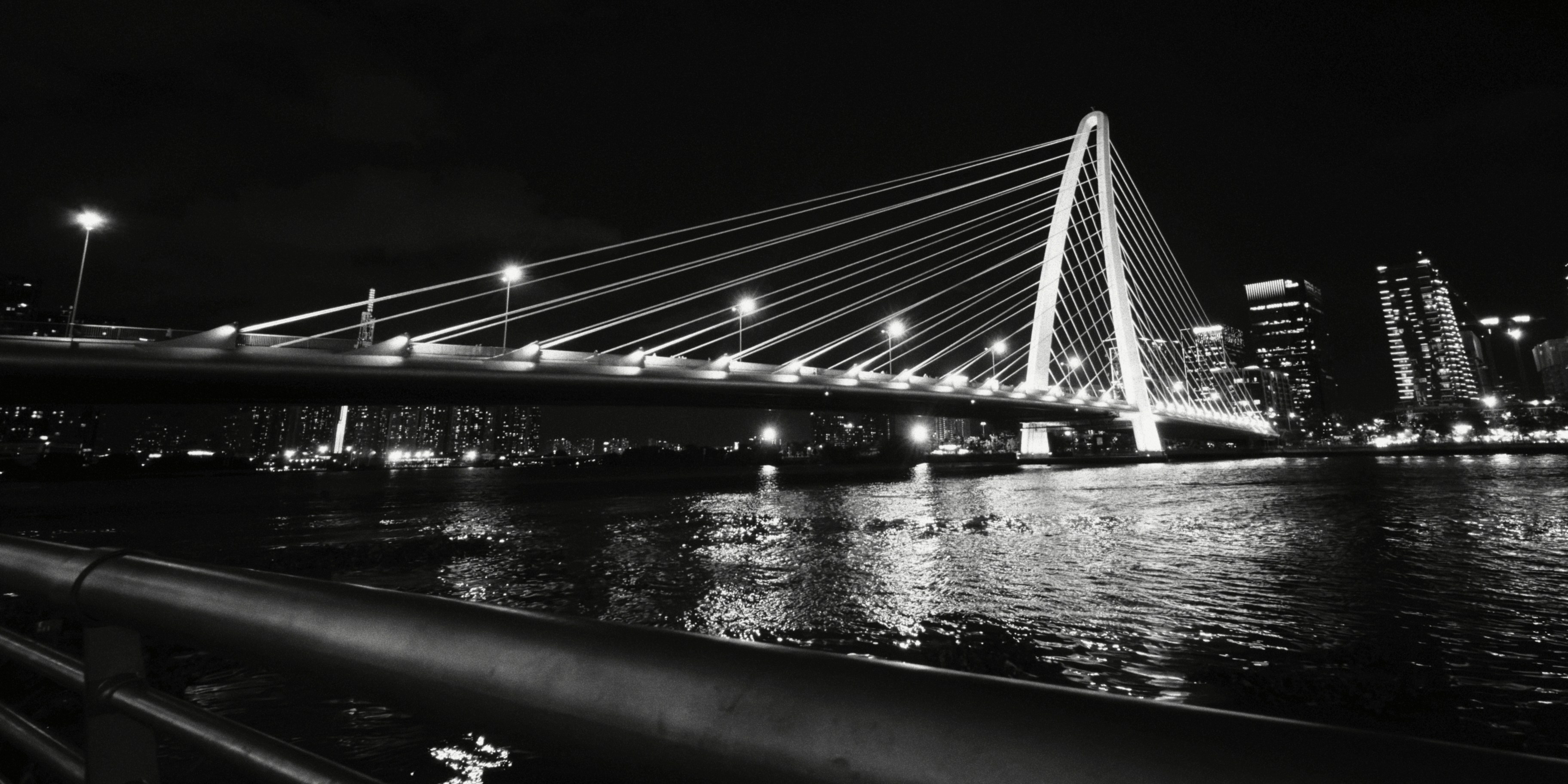 A cable-stayed bridge illuminated at night over a dark river with city lights
