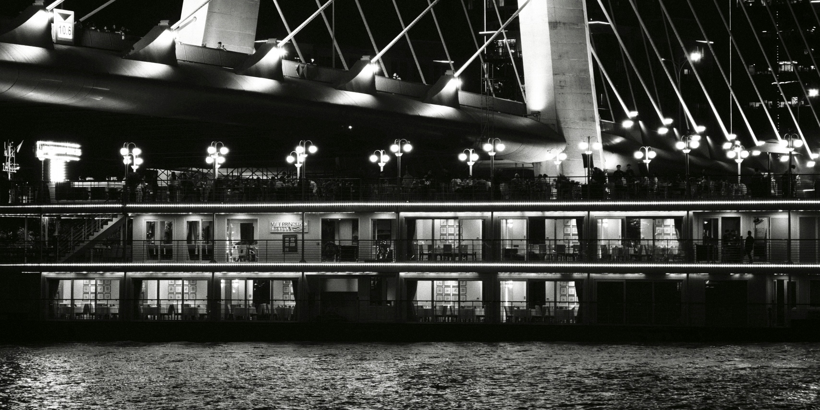 A multi-level river cruise boat illuminated at night beneath a large cable-stayed bridge