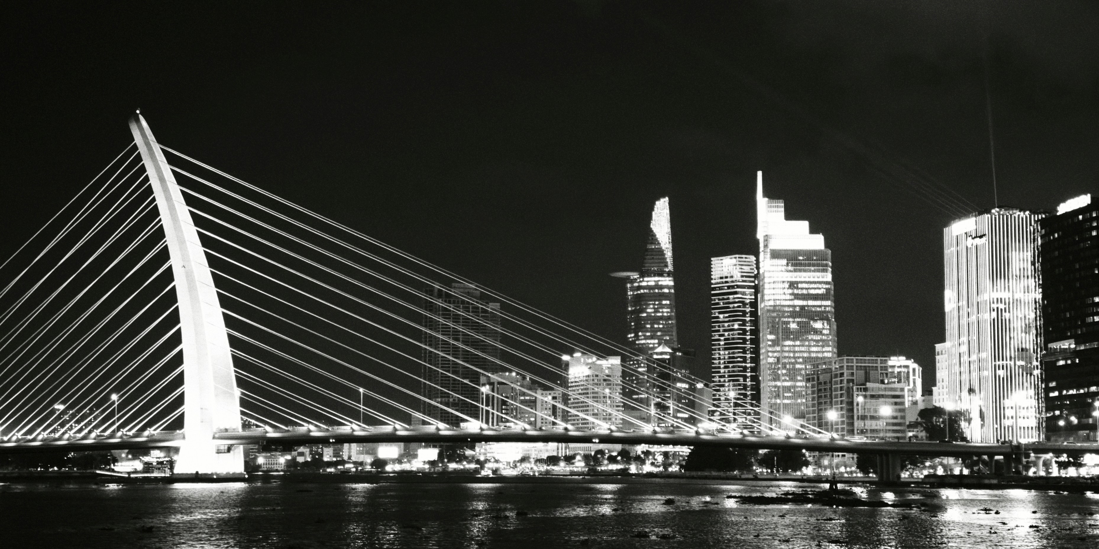 A cable-stayed bridge spanning a river below a city skyline in black and white