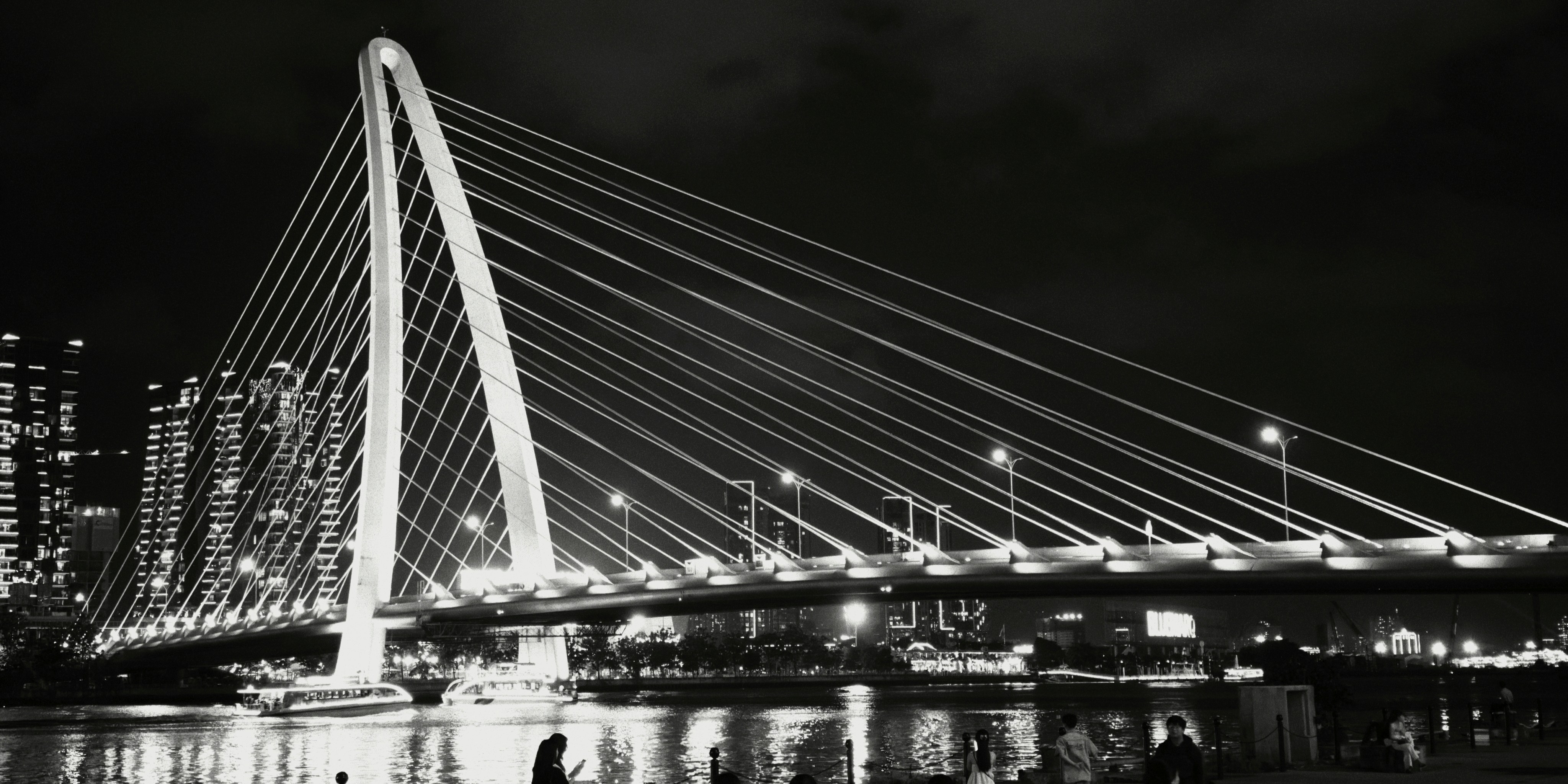 A cable-stayed bridge illuminated at night over a river with city buildings
