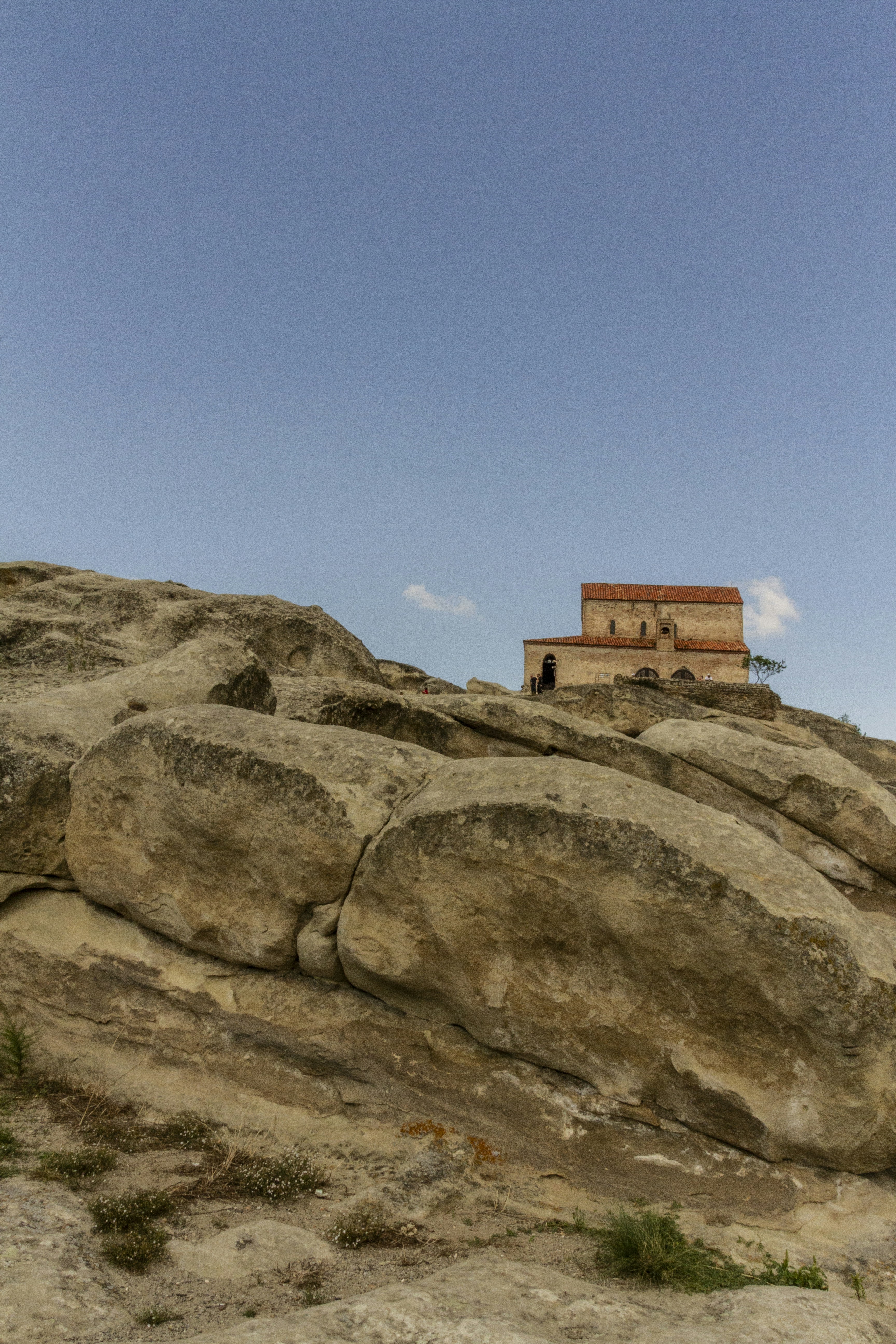 A stone church with a red tile roof atop a rocky hill