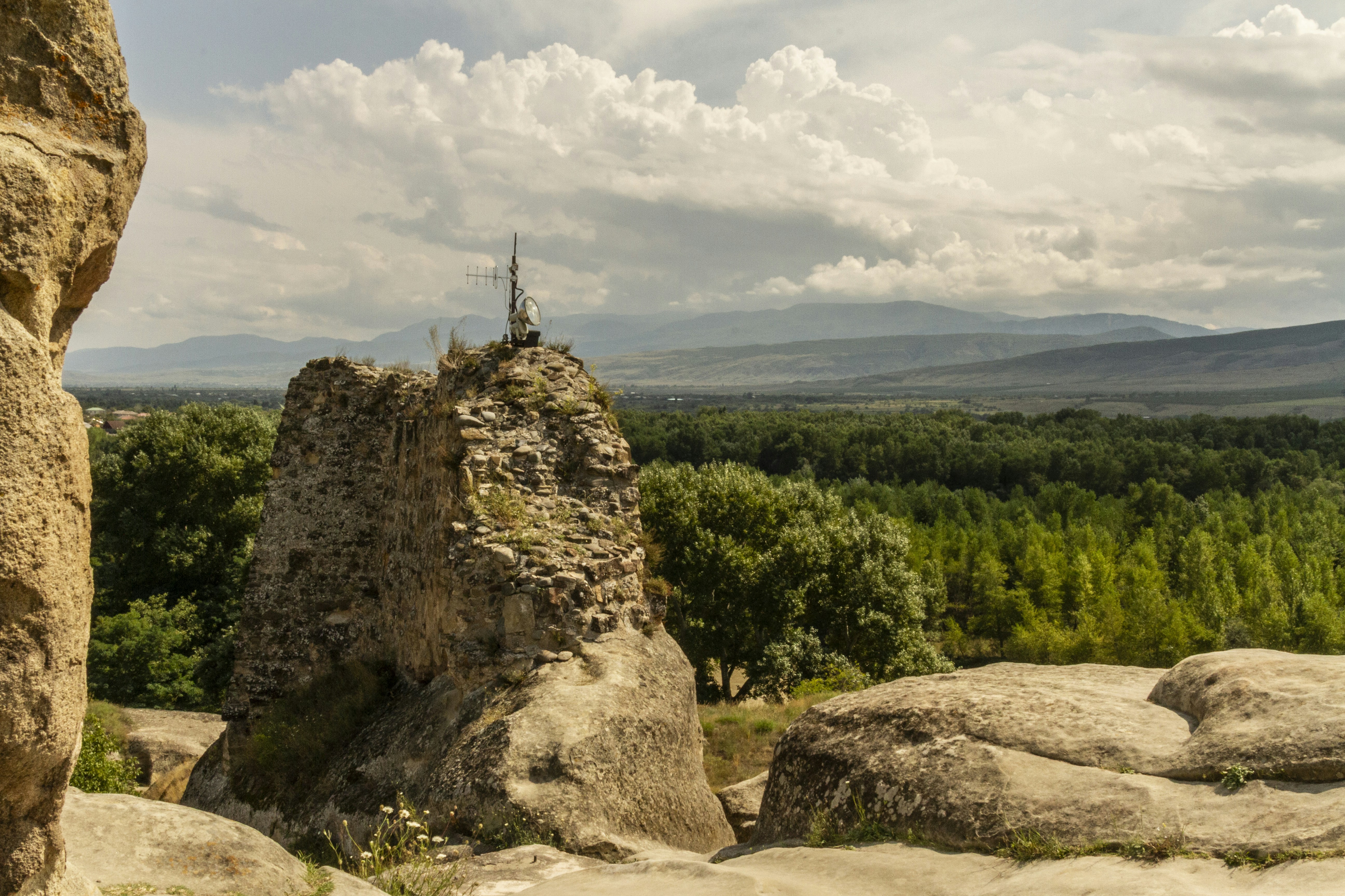 A stone ruin with an antenna on top overlooking a green valley