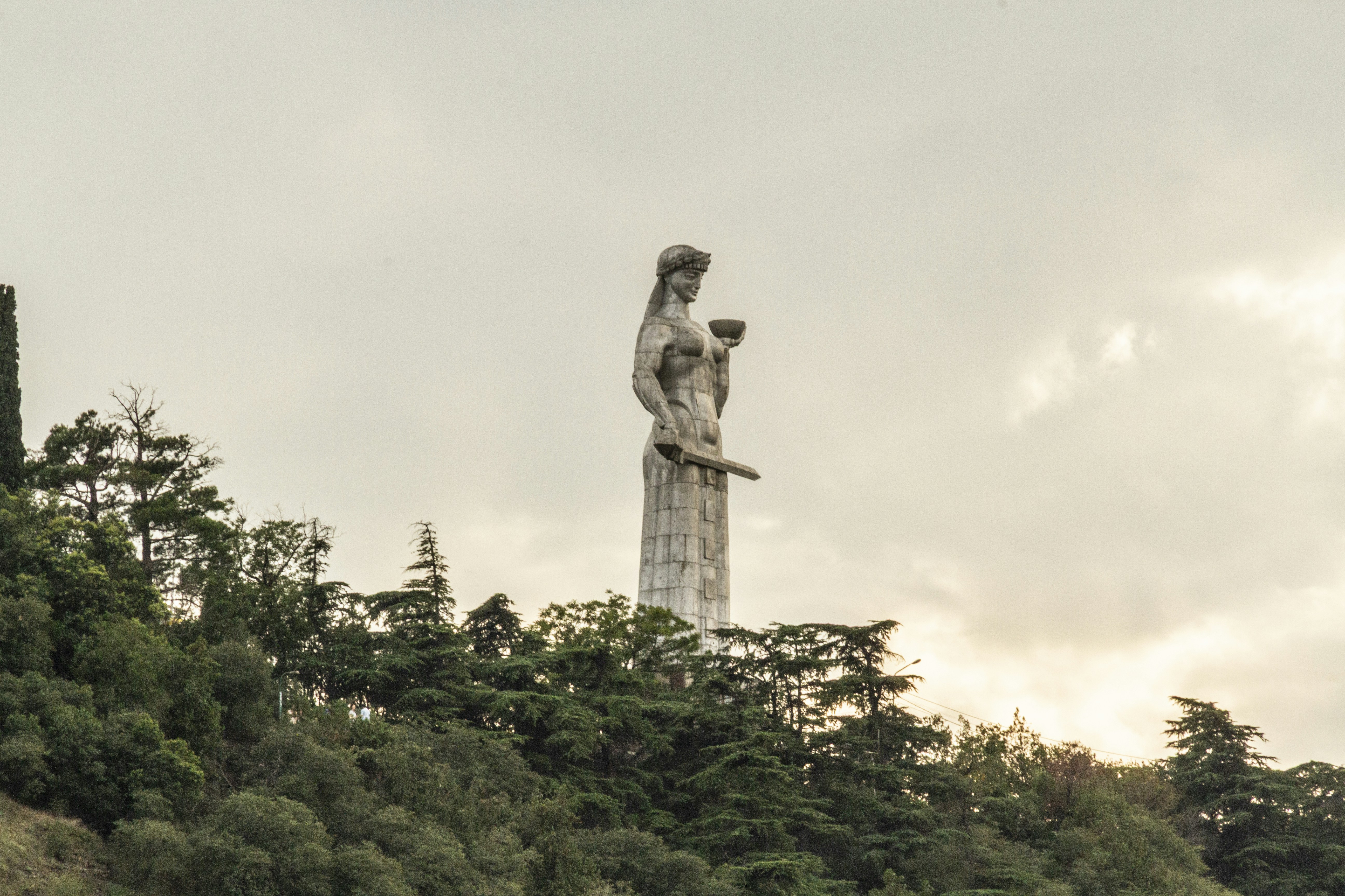The Mother of Georgia statue holding a sword and bowl above green trees