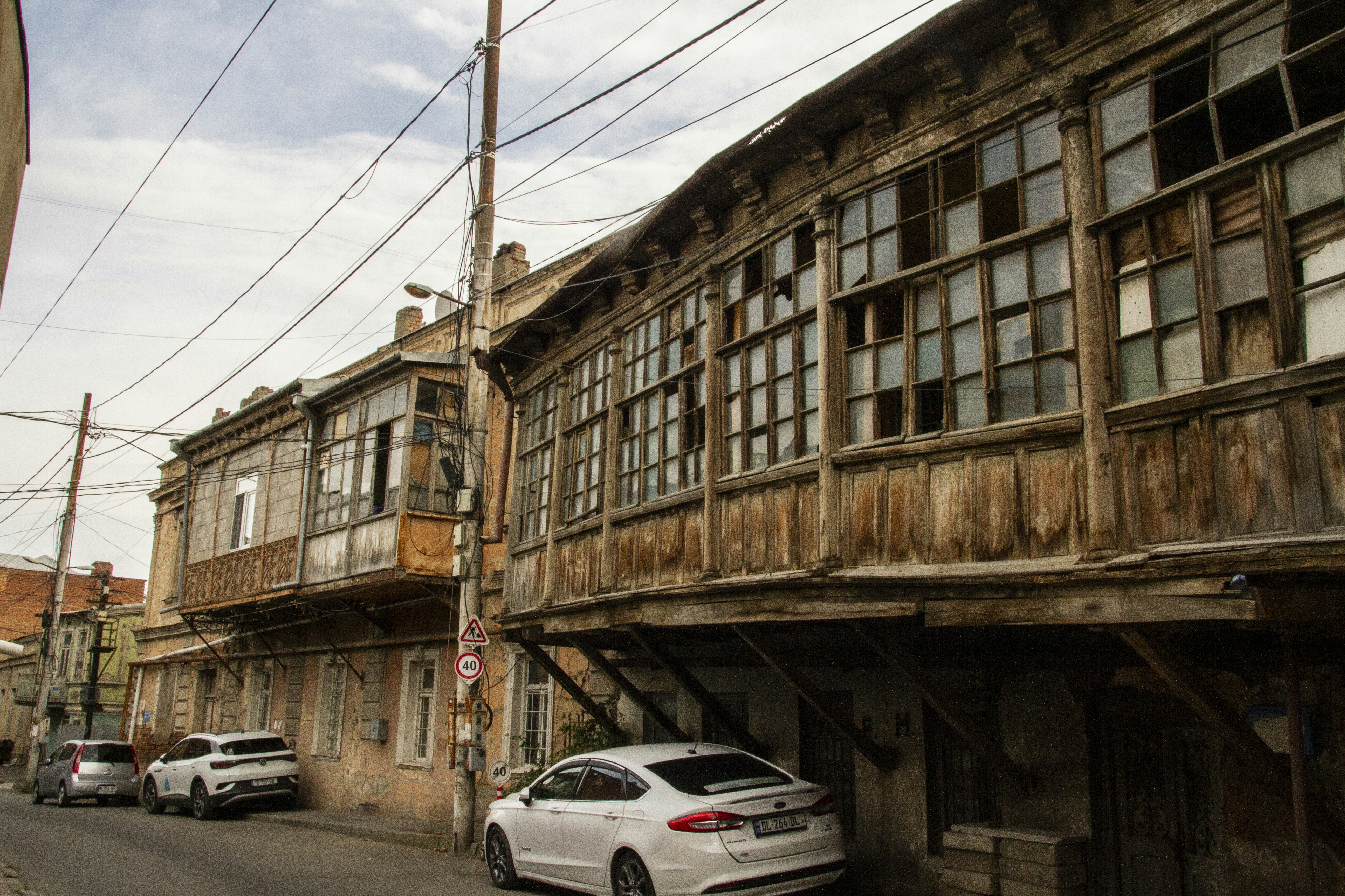 Old wooden balconies on a weathered building above parked cars on a street