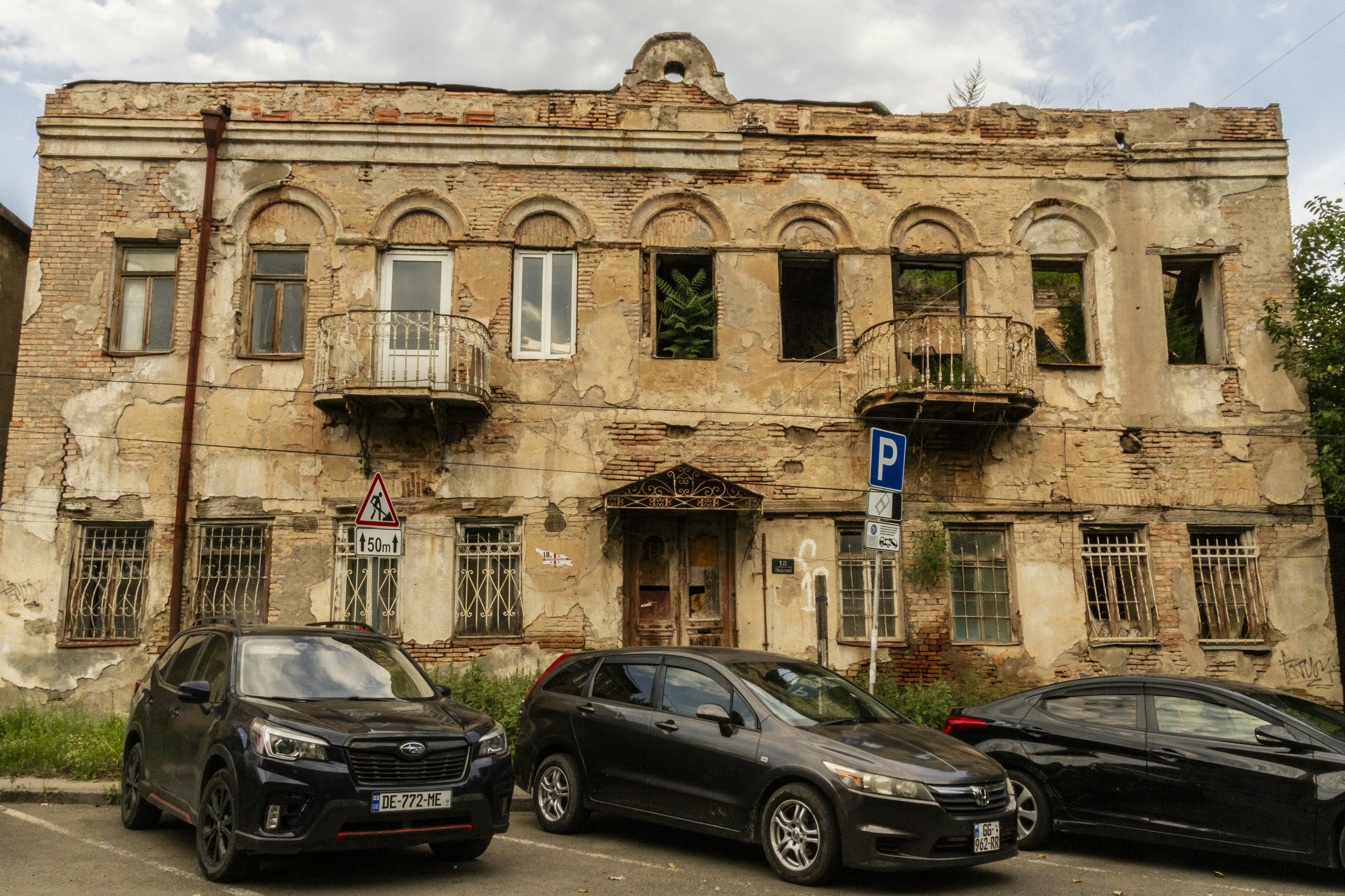 Cars parked in front of a weathered brick building with crumbling plaster and balconies