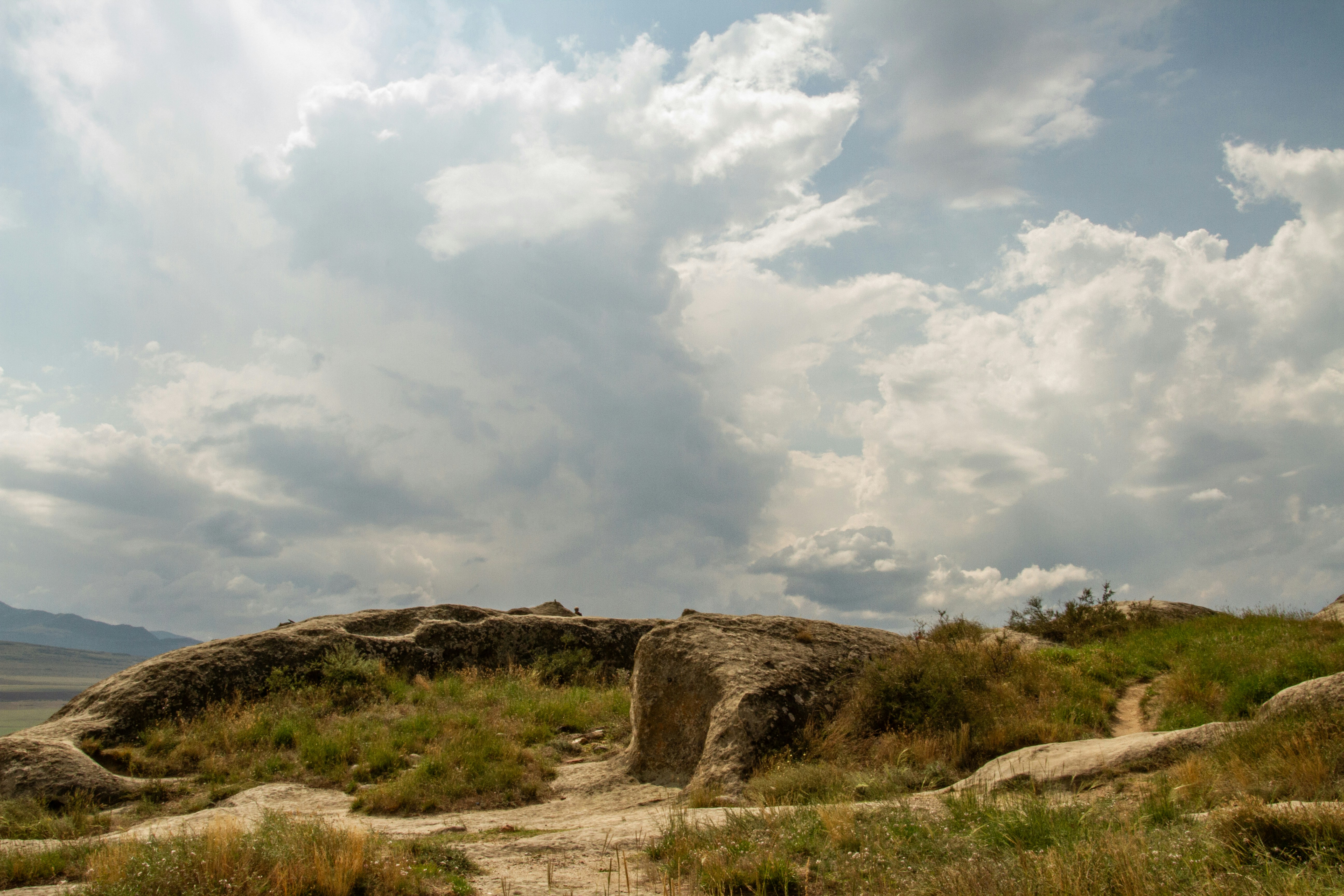 Large weathered rock formations on a grassy hillside under a cloudy sky