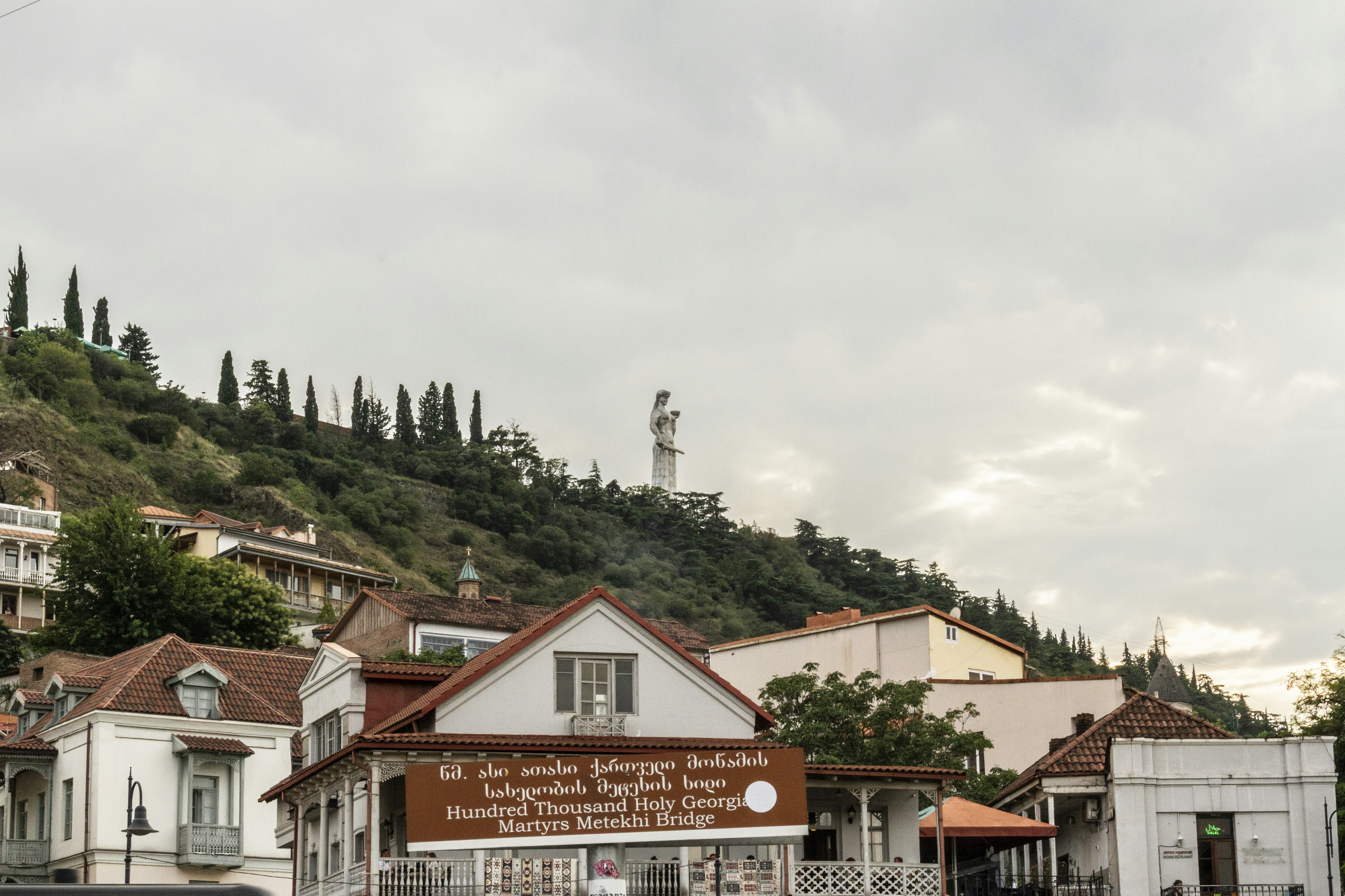 The Kartlis Deda statue on a green hill above buildings in Tbilisi, Georgia