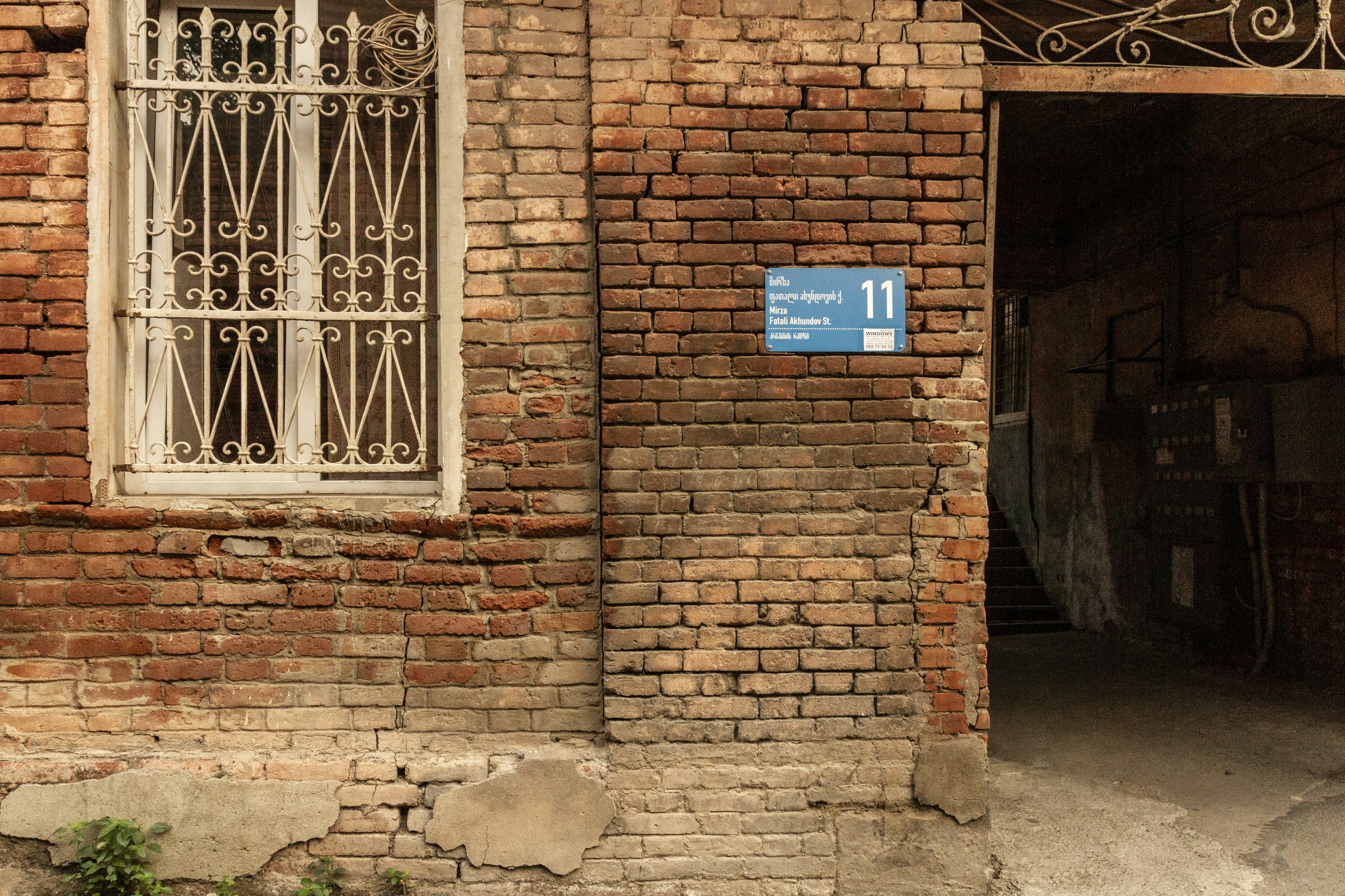 A red brick wall with a window and a blue street sign in Tbilisi
