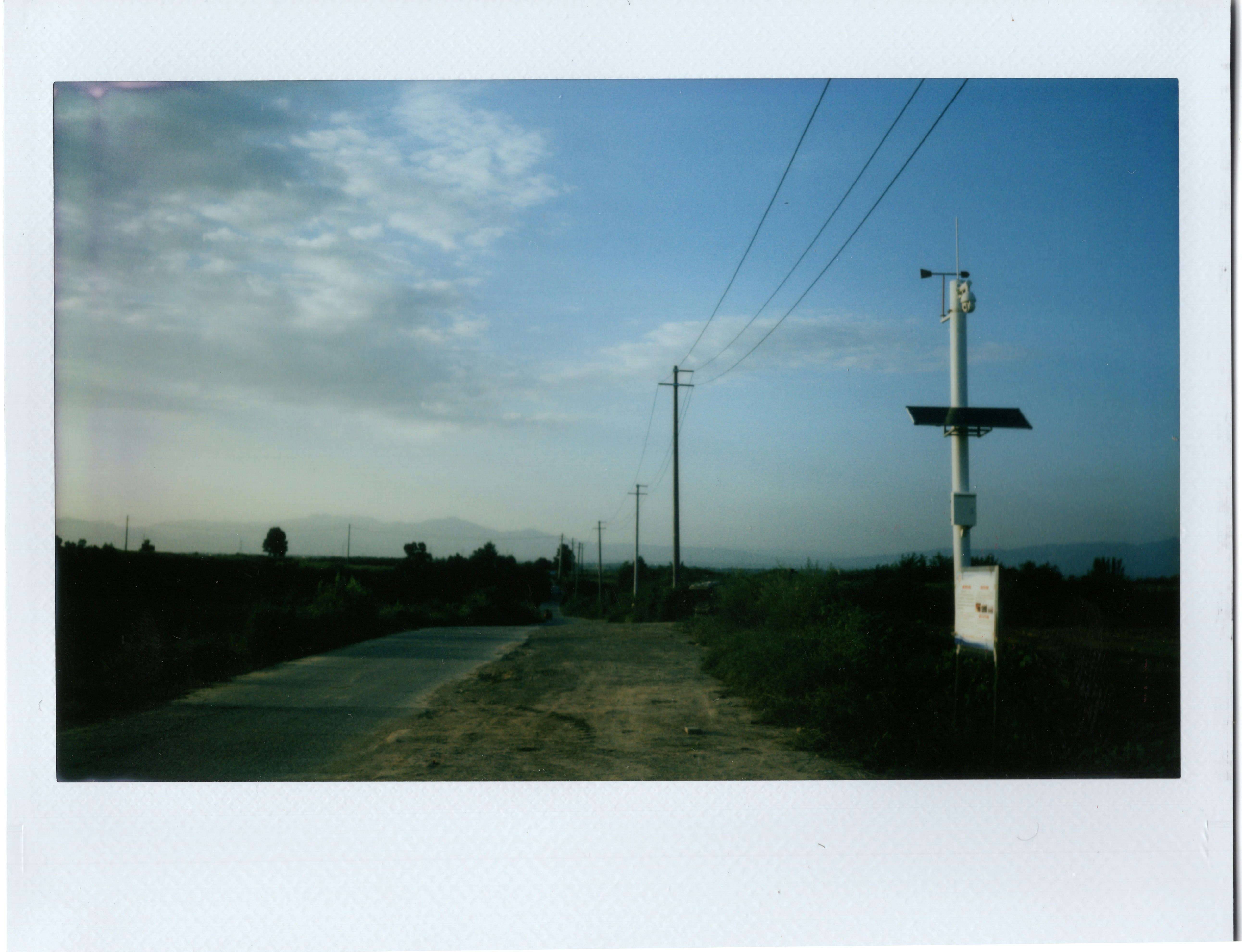 A rural road with utility poles and a solar-powered weather station