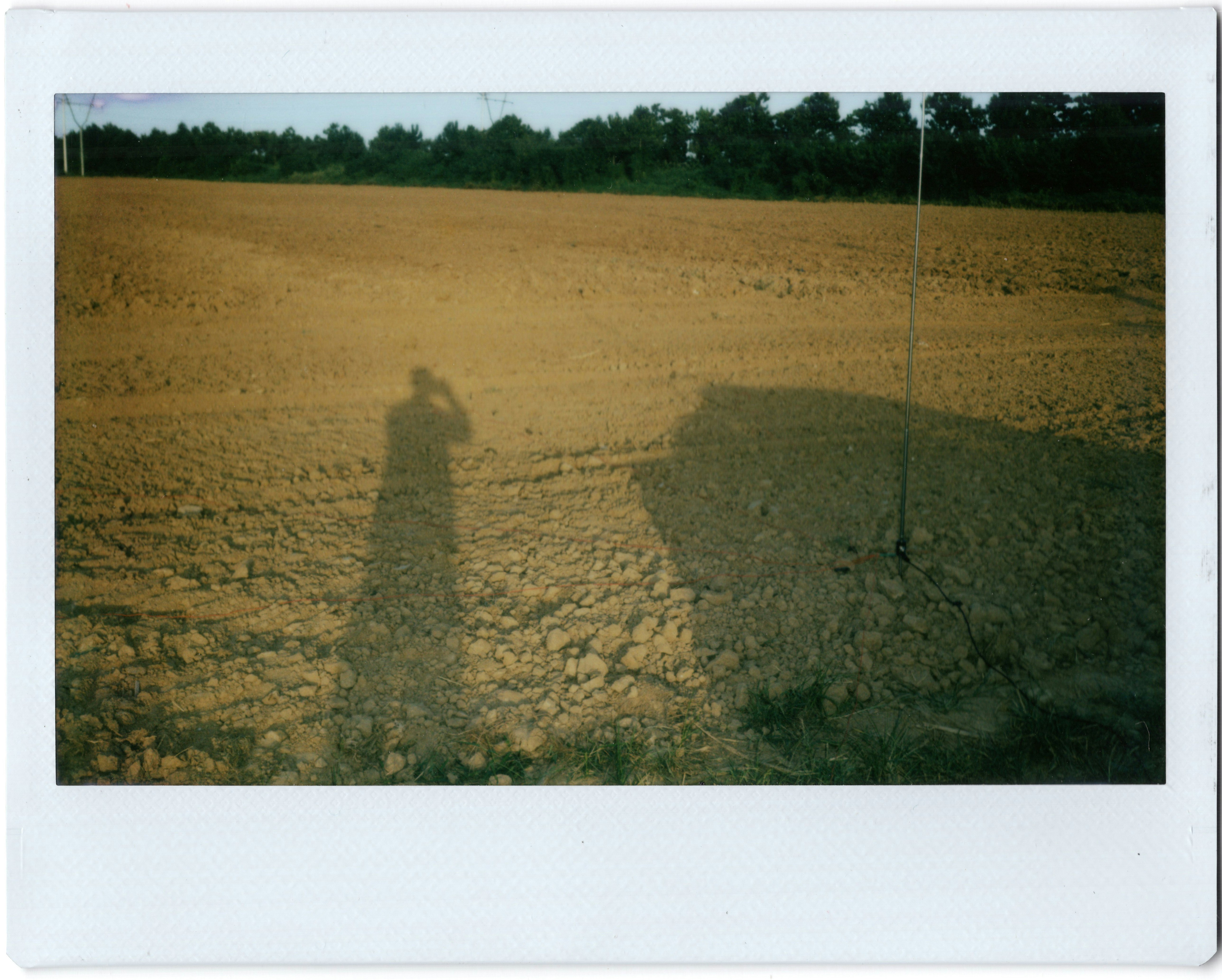 A long shadow of a person holding a camera on a plowed field