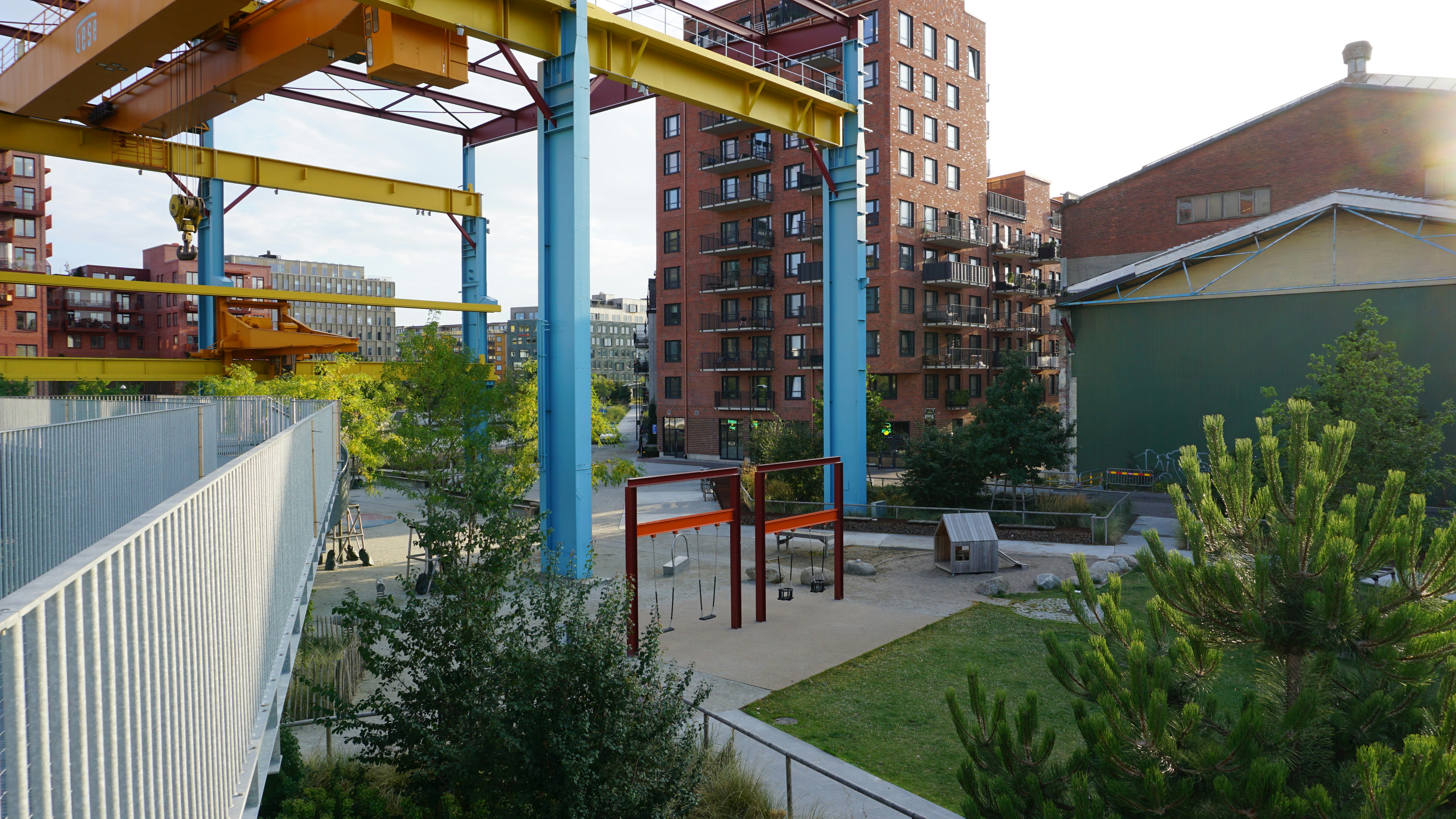 A playground with swings and a small wooden house beneath a large yellow crane