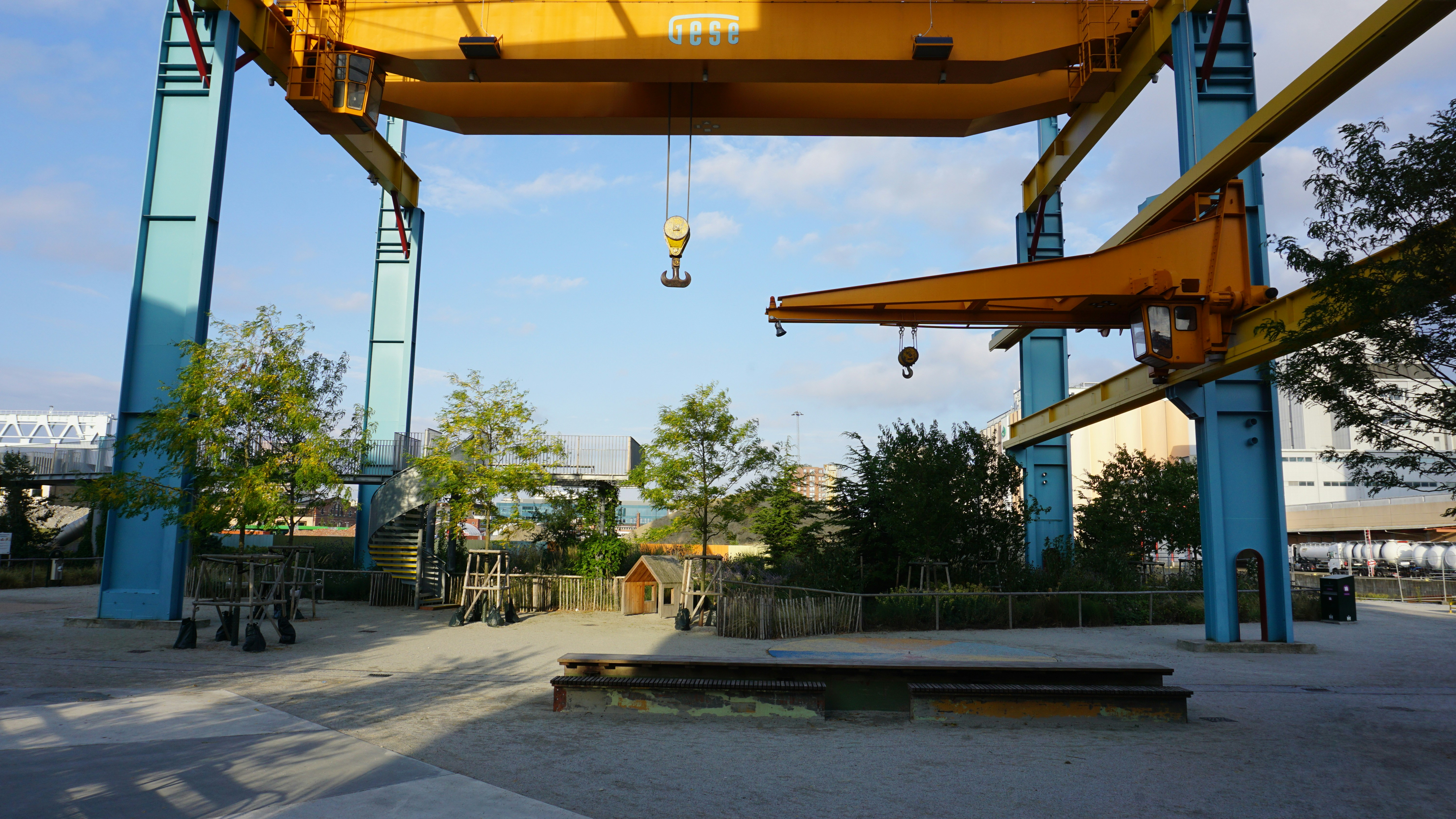 A large yellow industrial crane spanning a public park with trees and paths