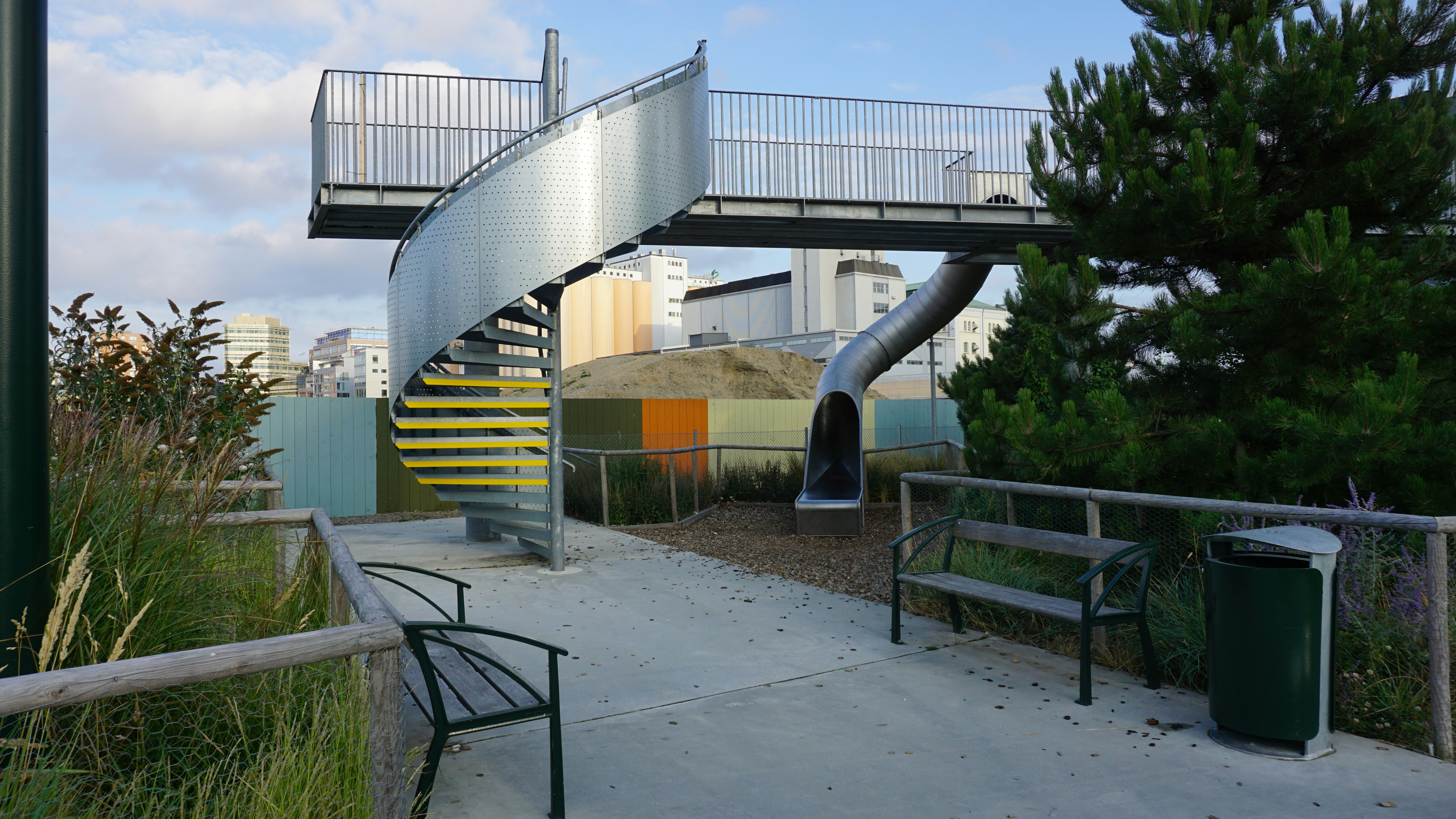 A metal spiral staircase and slide on an elevated walkway in a park