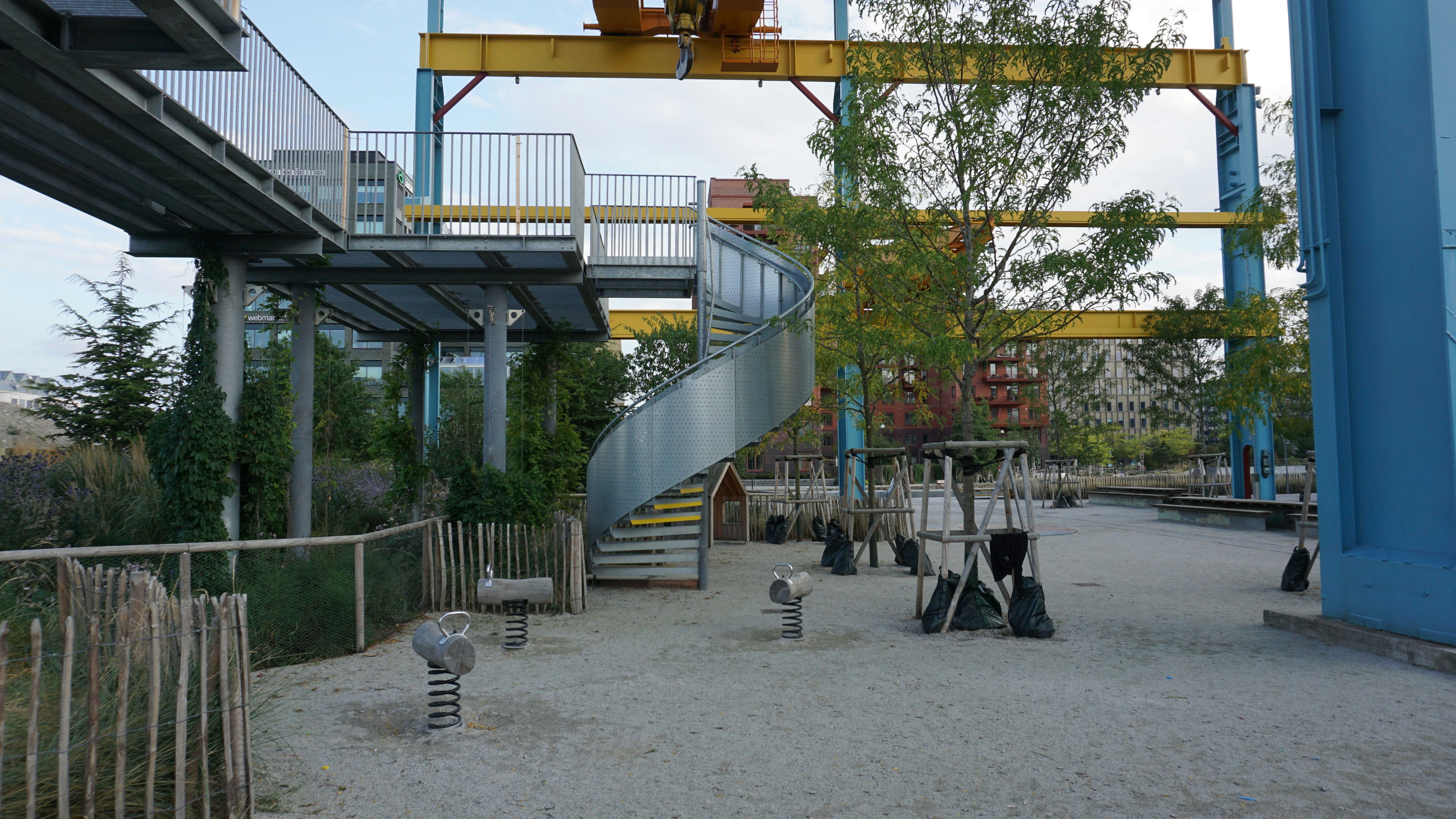 A metal spiral staircase and elevated walkway in a park with playground equipment