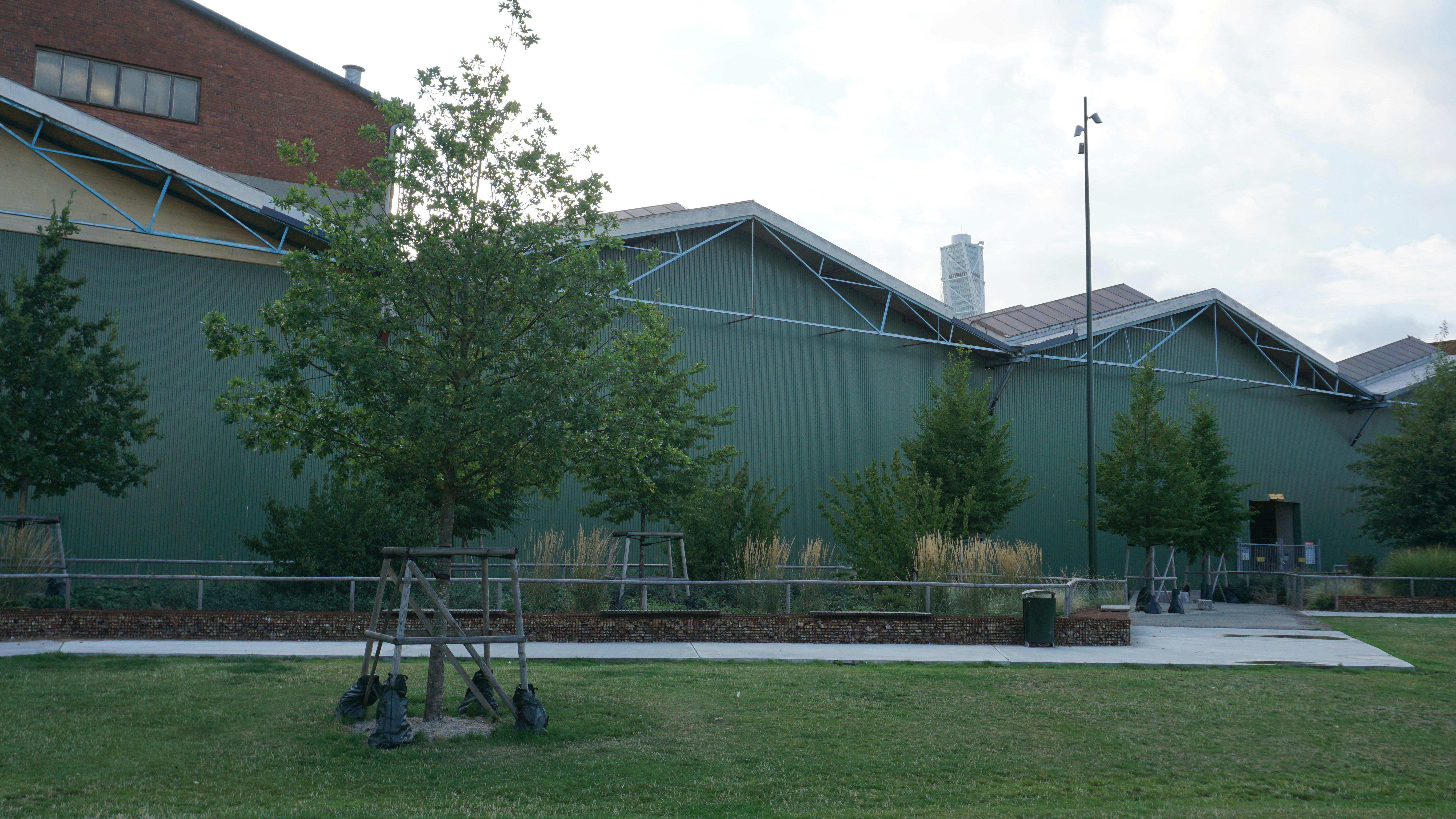 A green industrial building with a sawtooth roof behind a grassy park area
