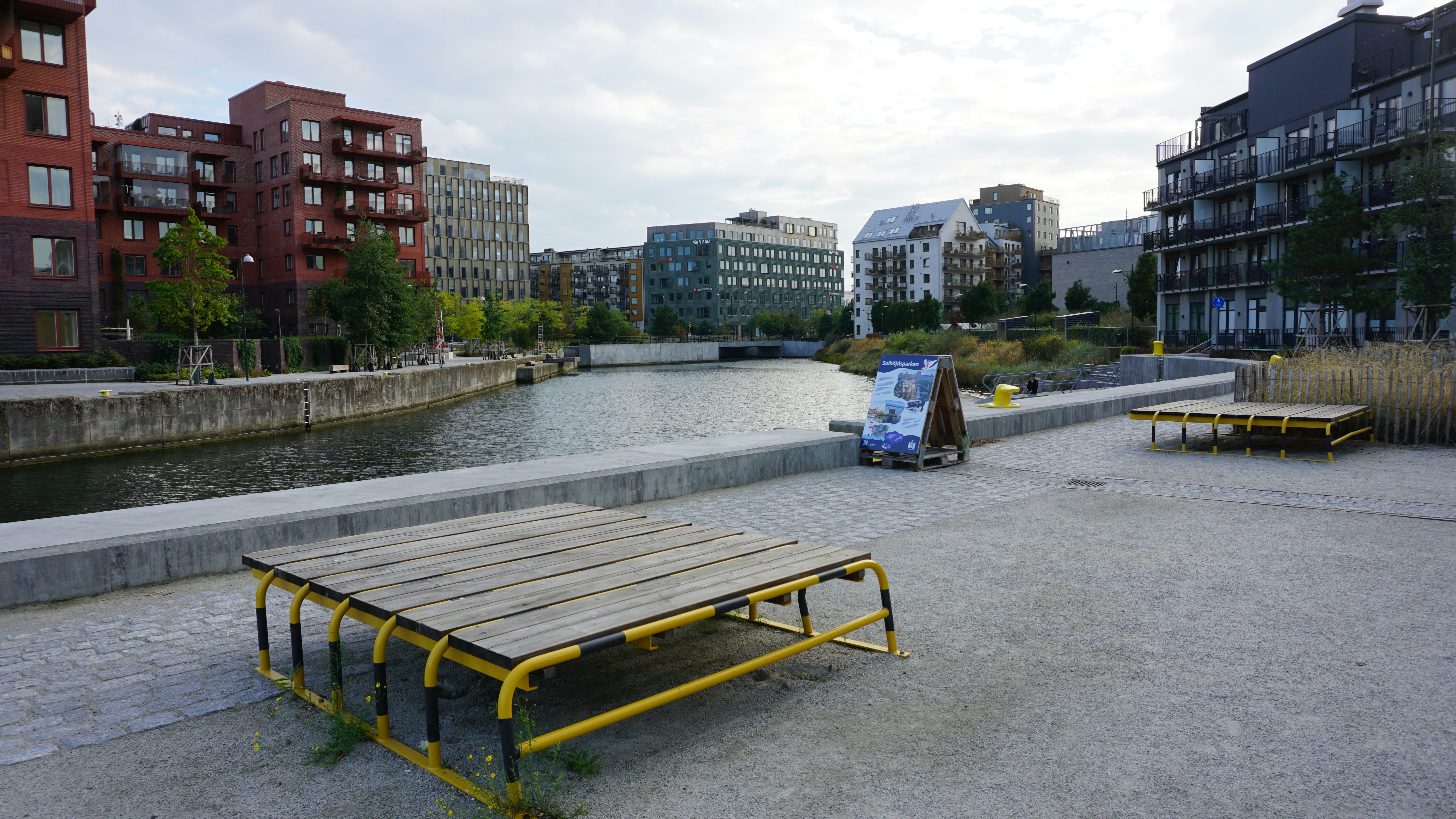 Wooden platforms with yellow metal frames along a canal in a modern city