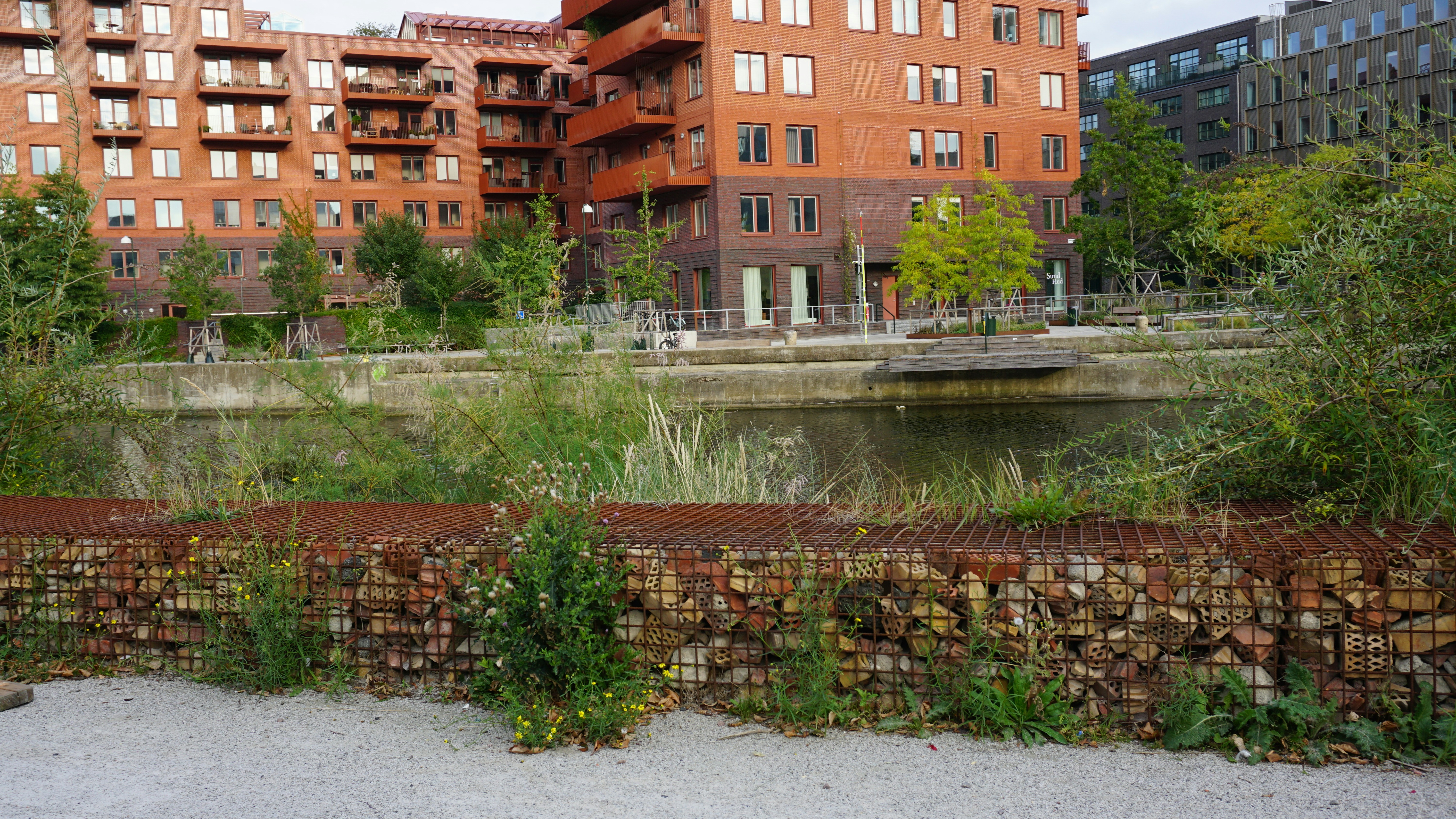 A gabion wall filled with bricks beside a canal and red brick apartment buildings