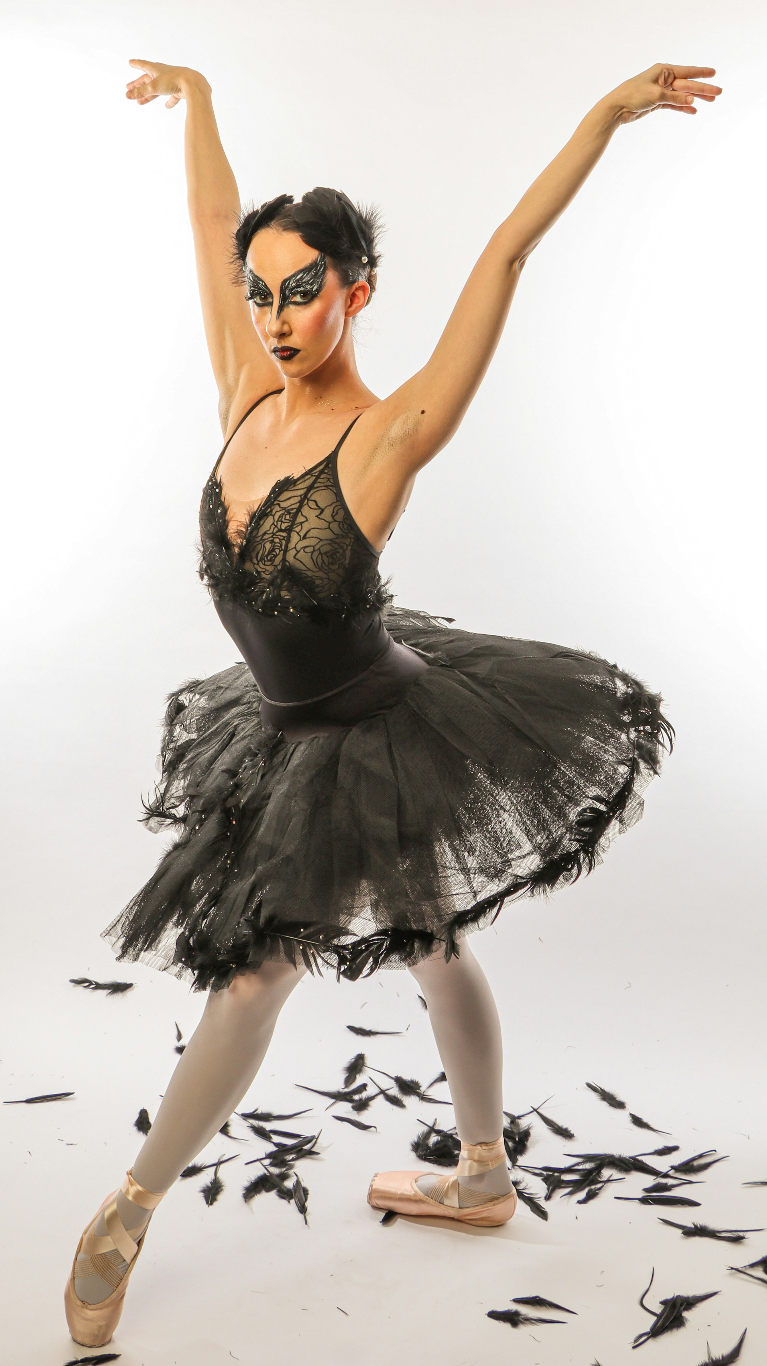 Eine Ballerina in schwarzem Tutu und gefiedertem Kopfschmuck, die mit verstreuten schwarzen Federn posiert