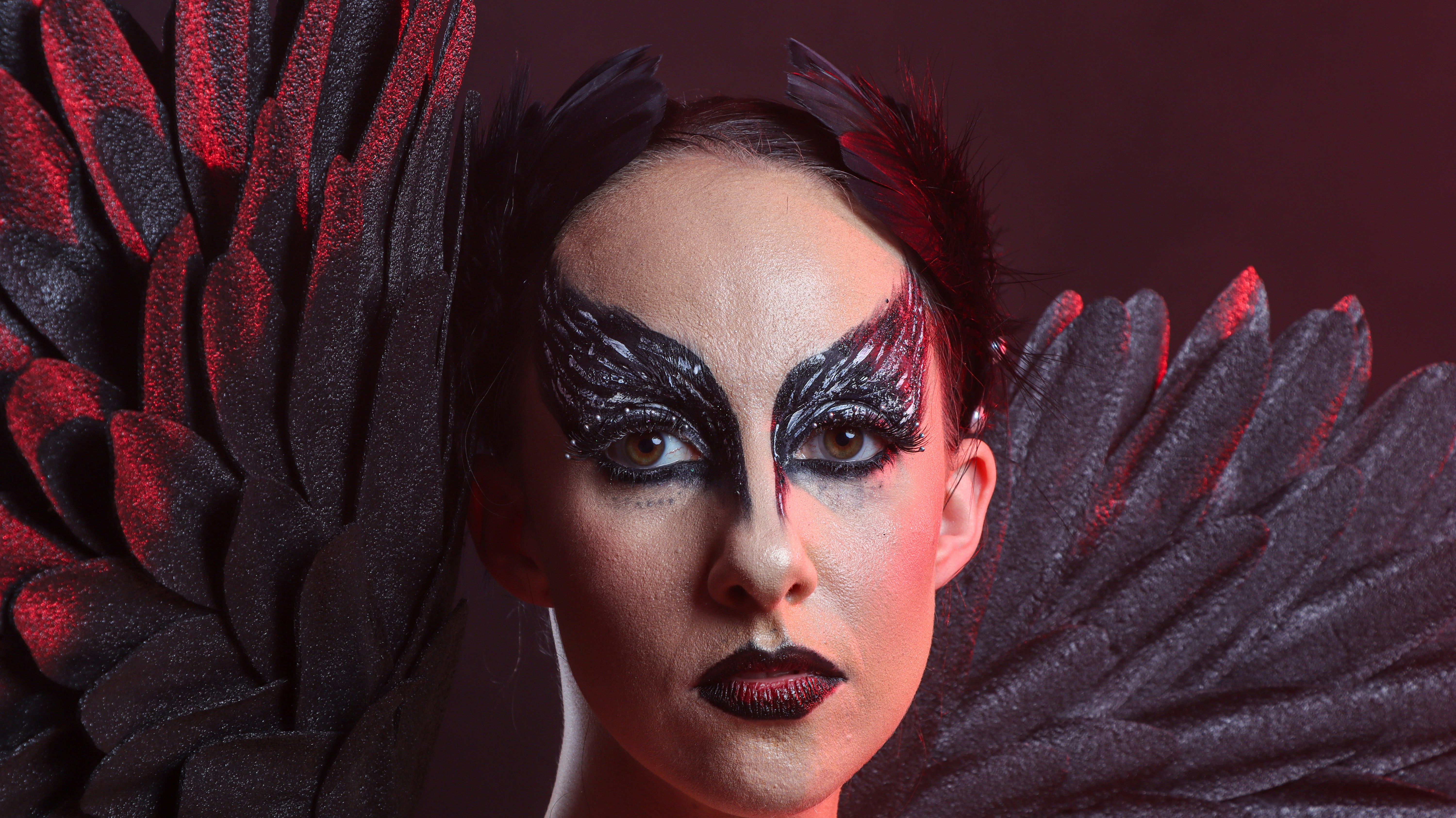 Eine Person mit schwarzen Federflügeln und dramatischem schwarzen Augen-Make-up