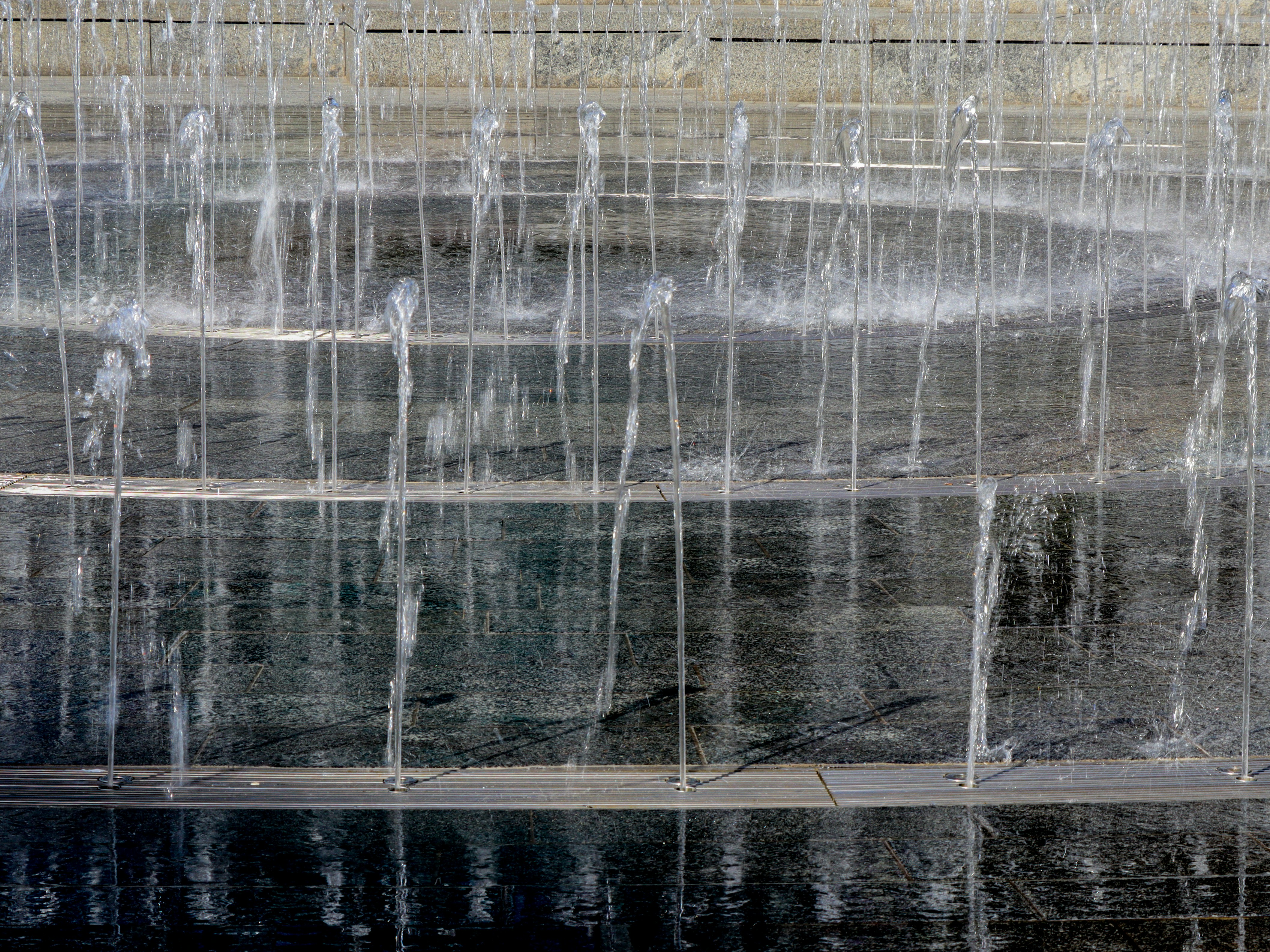 Vertikale Wasserstrahlen, die aus einem dunklen Granitbrunnenbecken aufsteigen