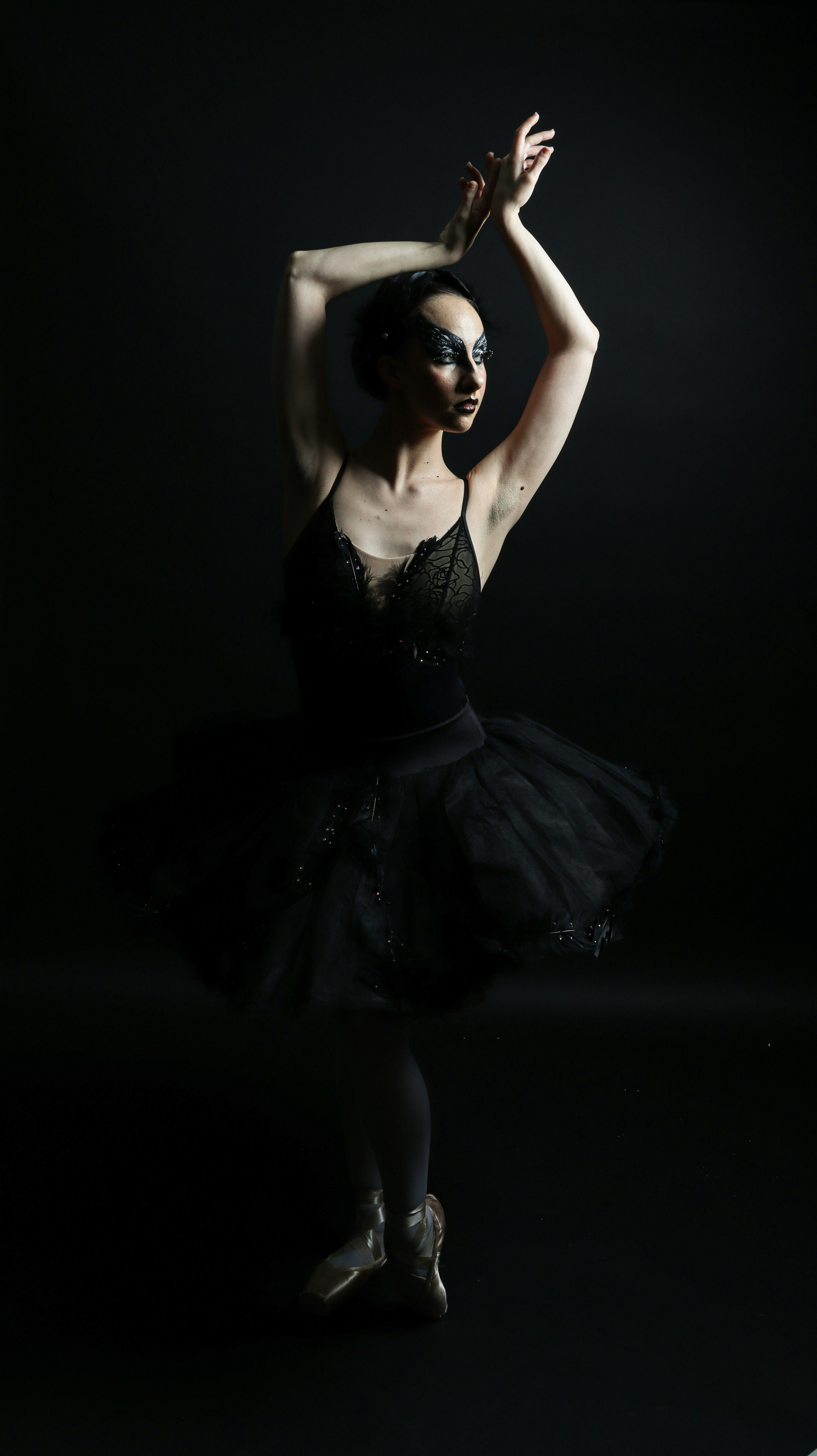 Eine Ballerina in einem schwarzen Tutu und Spitzenoberteil, die mit erhobenen Armen posiert