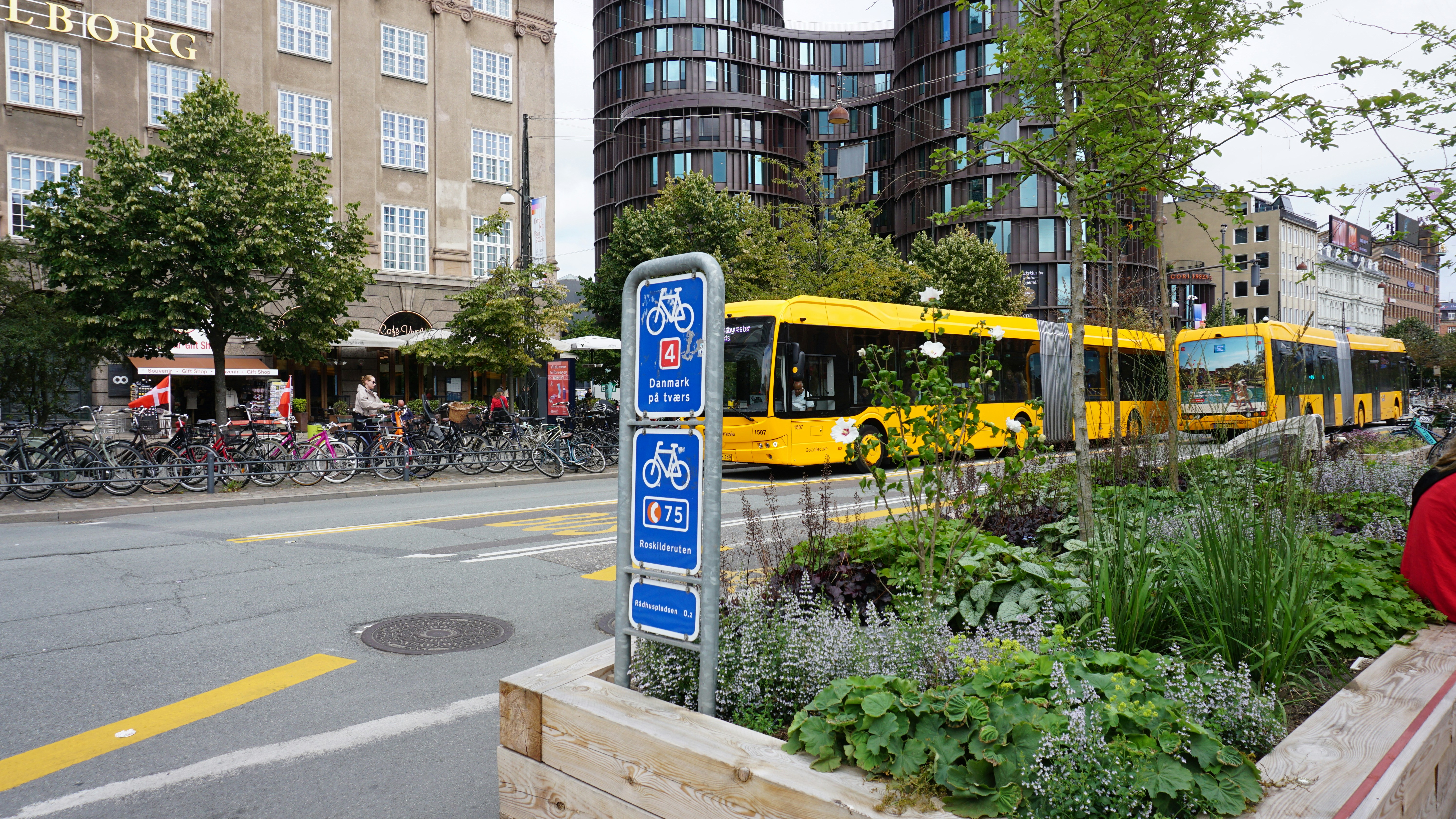 A yellow bus on a city street with bicycle signs and planters