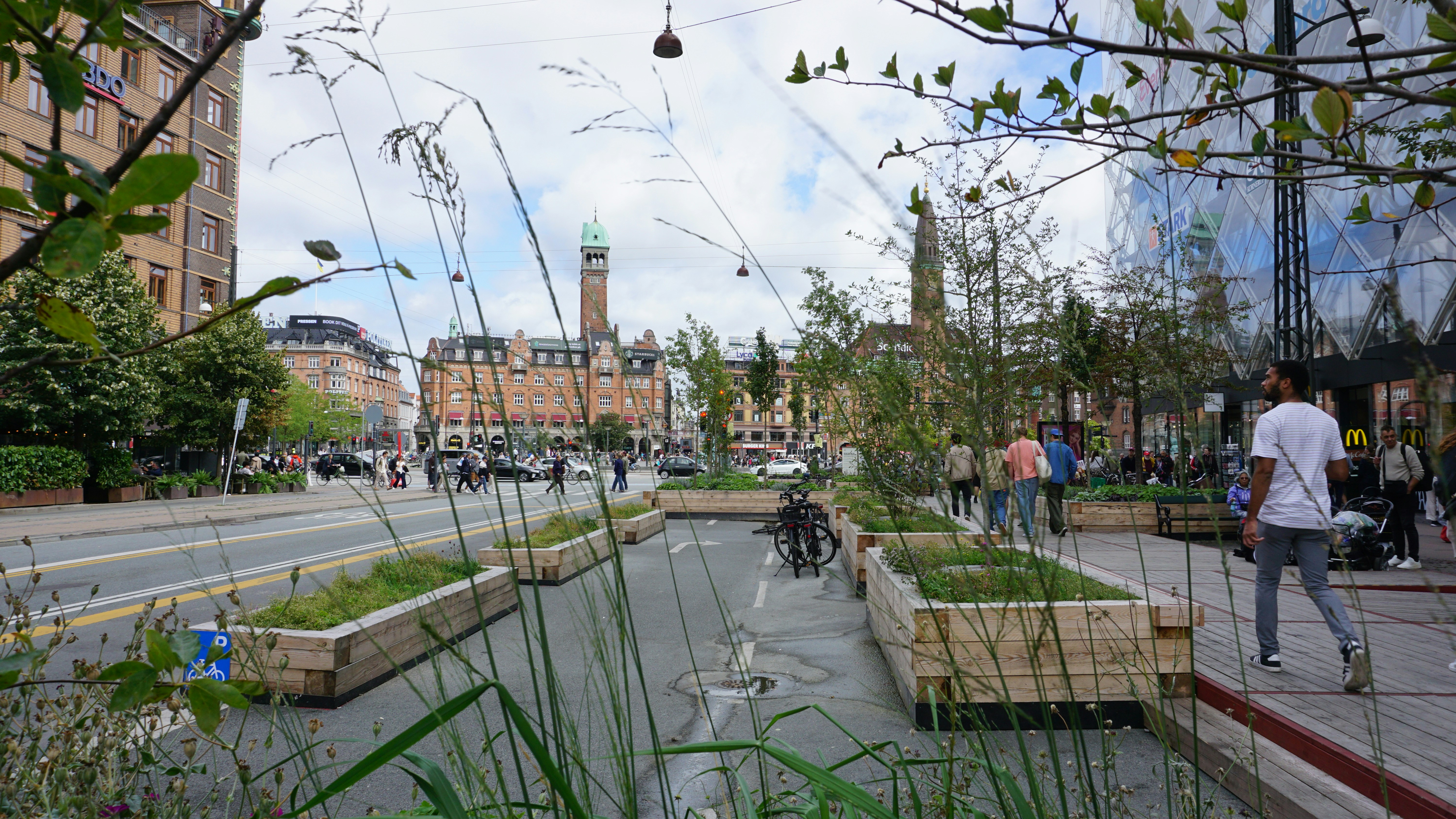 People walking on a city street with wooden planters and historic buildings in Copenhagen