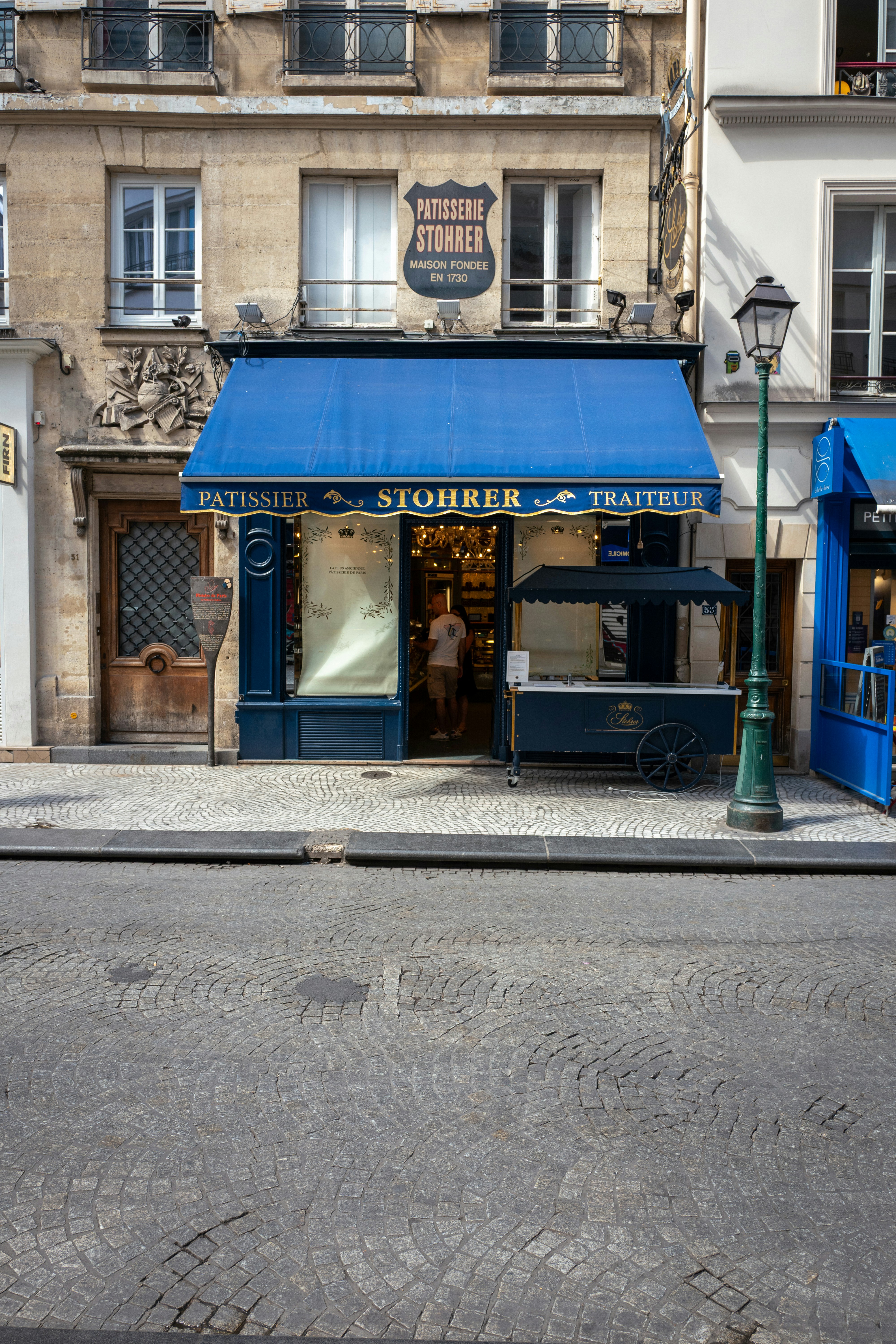 The Stohrer patisserie storefront with a blue awning on a cobblestone street in Paris