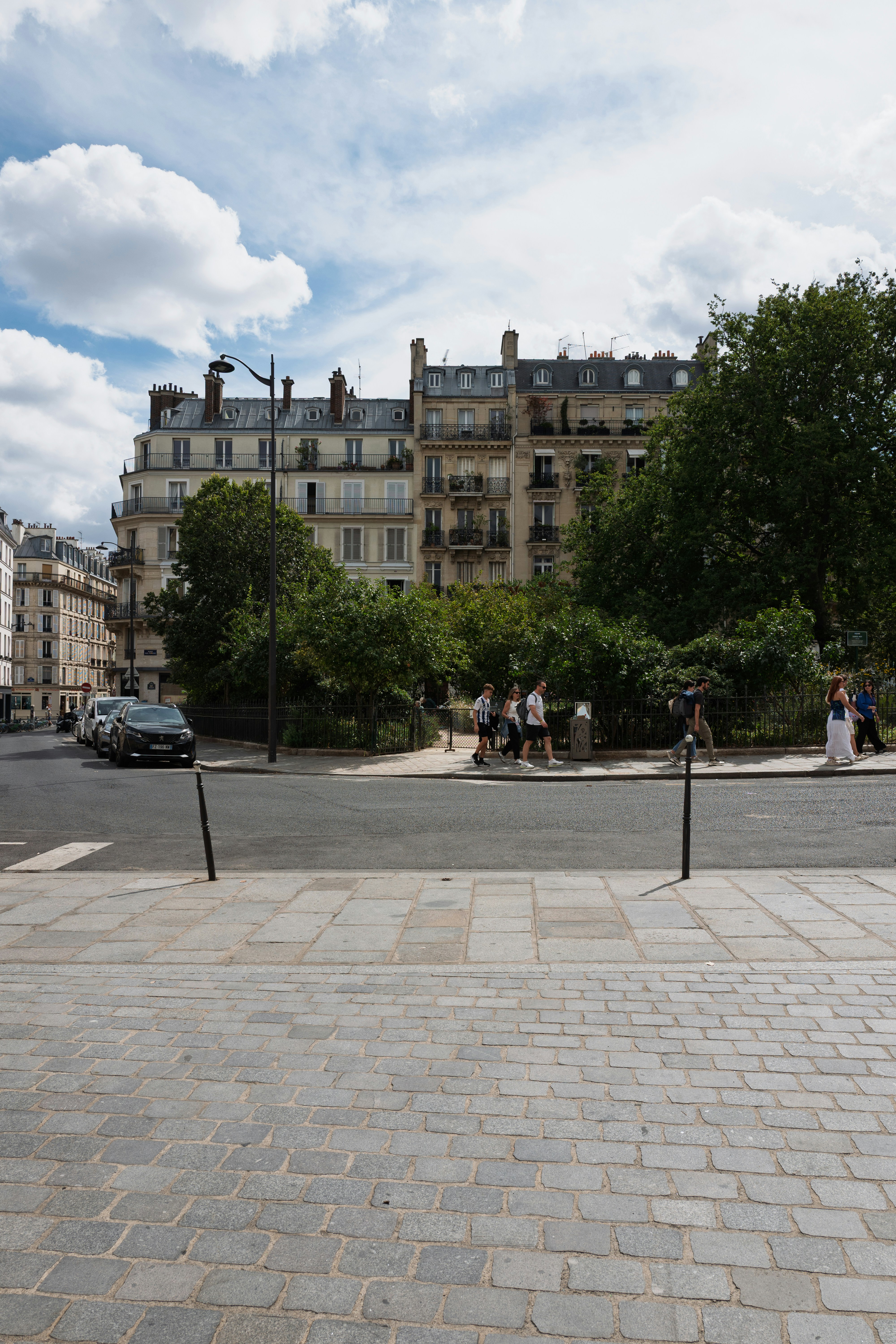 People walking on a sidewalk past a park and historic buildings in Paris