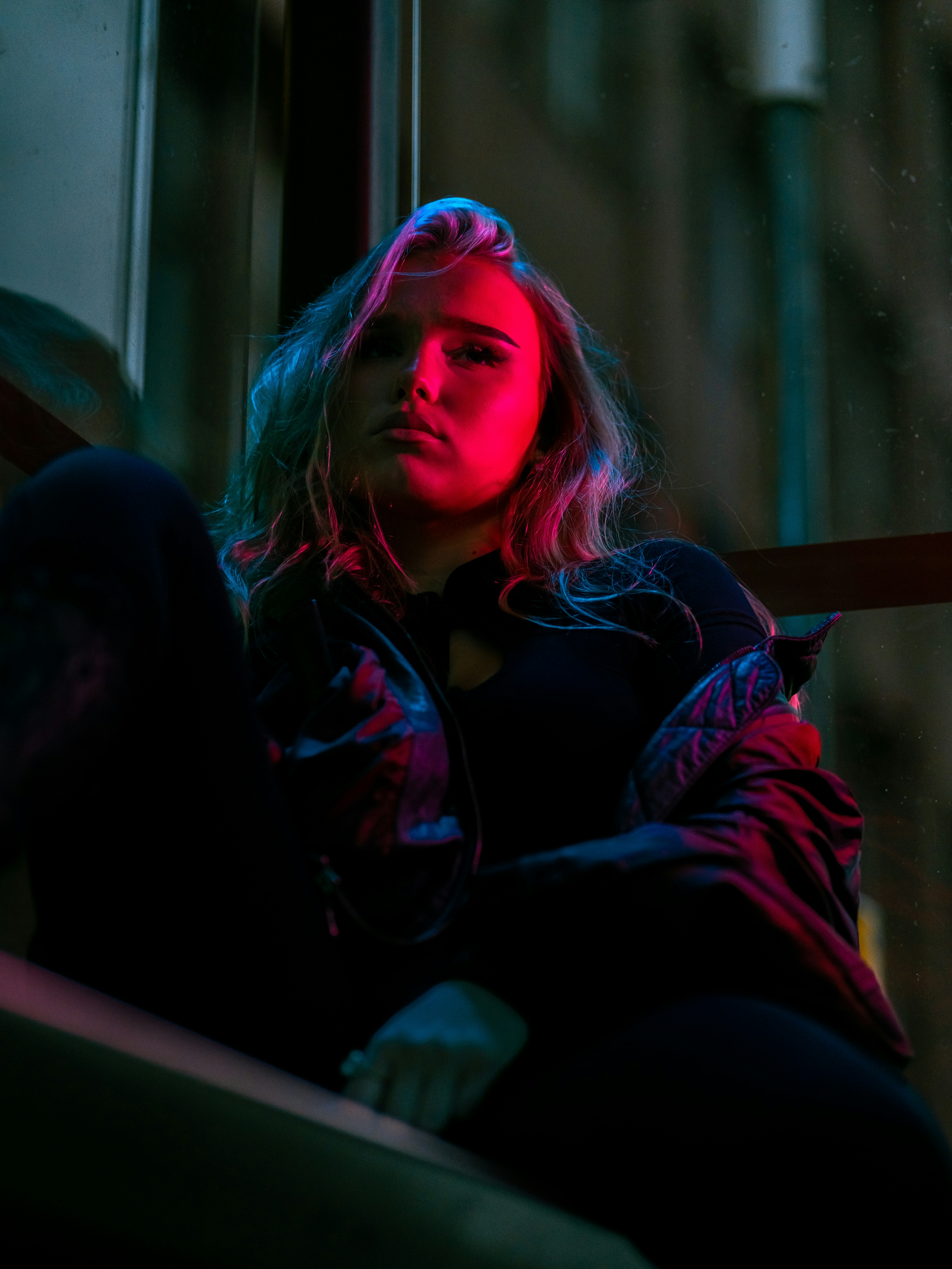 A woman in a black jacket lit by vibrant pink and blue light