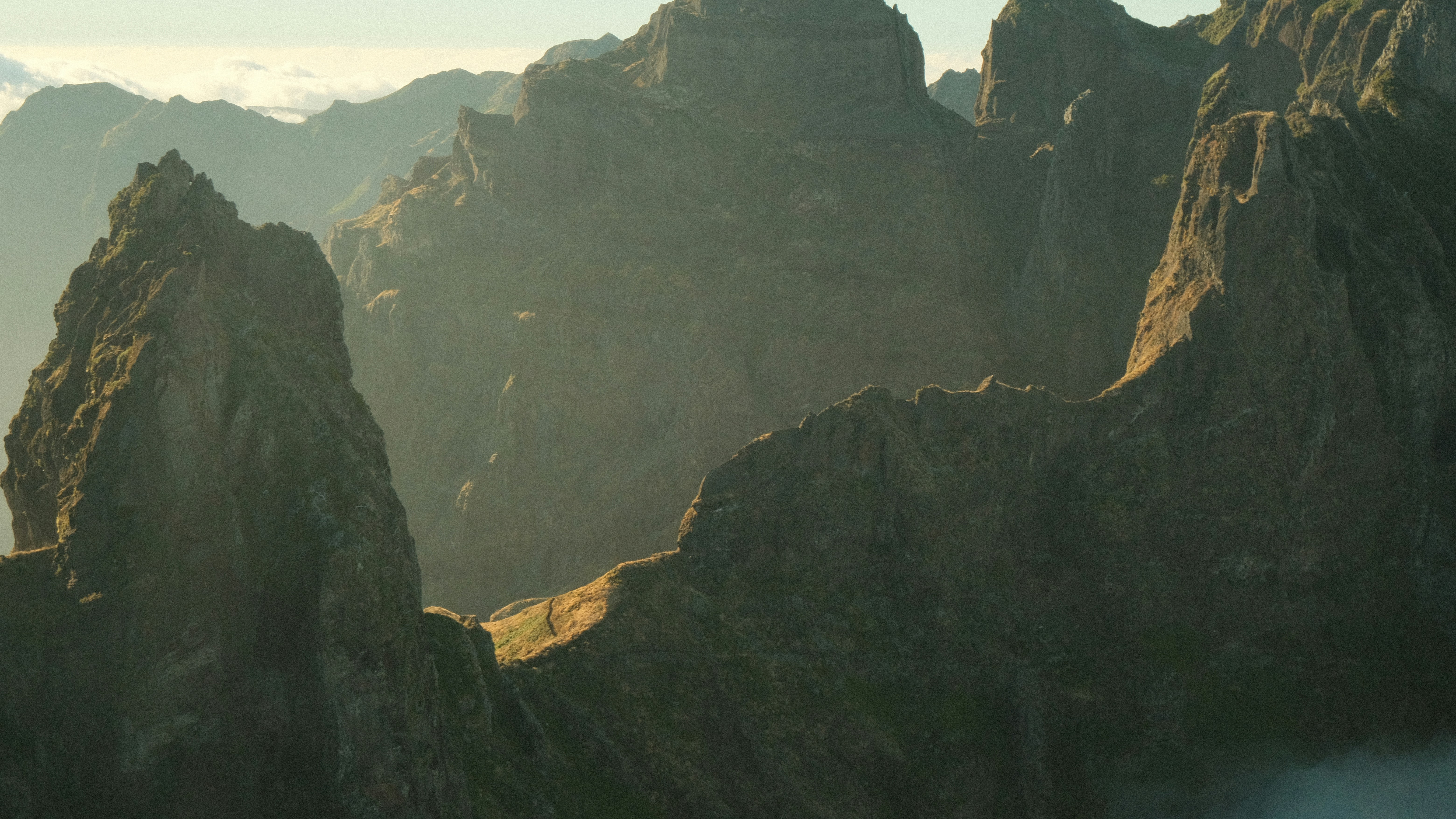 Cime montane frastagliate sotto una luce dorata fioca con ombre nelle valli profonde
