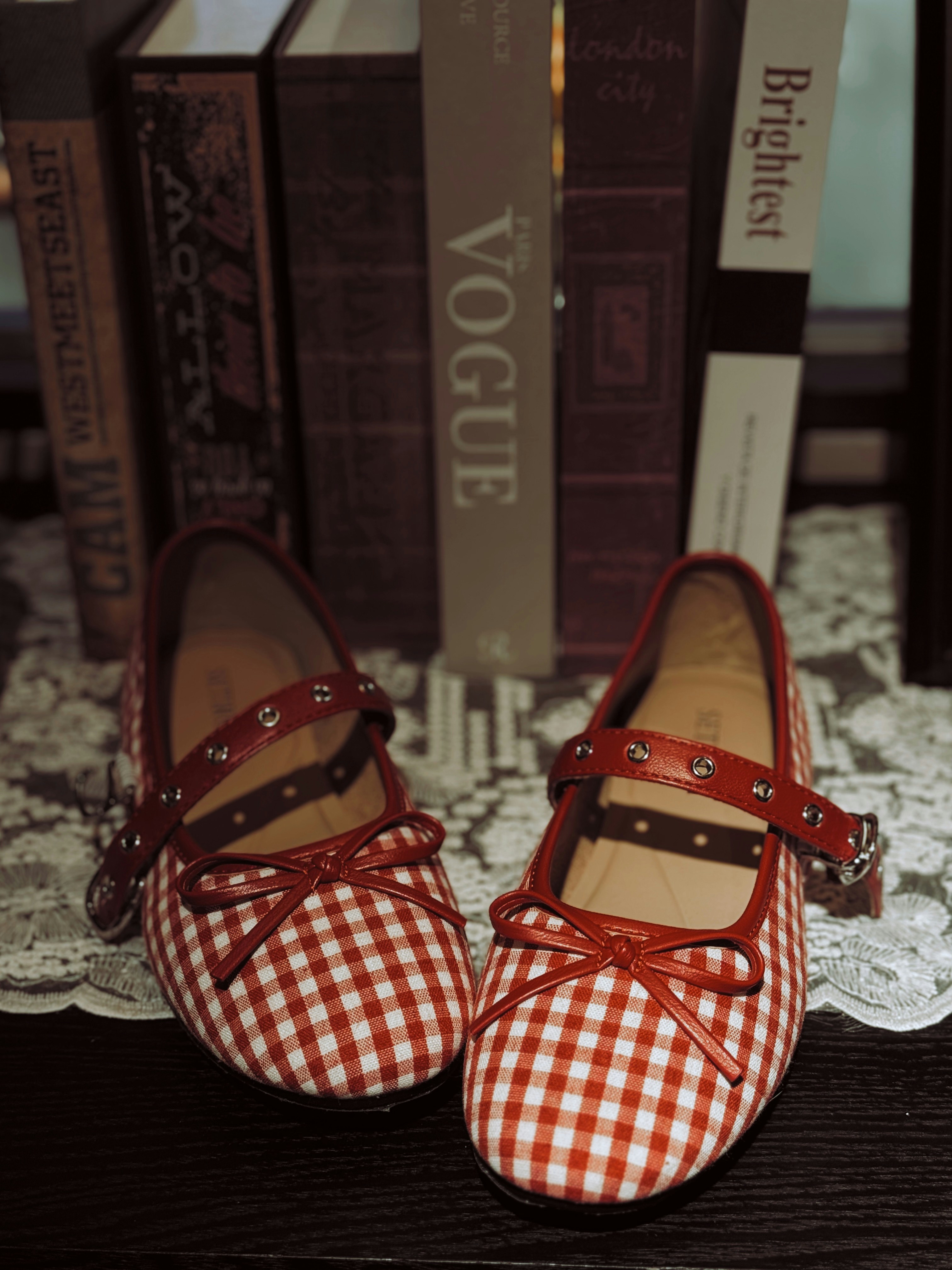 A pair of red and white gingham flats with bows on a lace doily