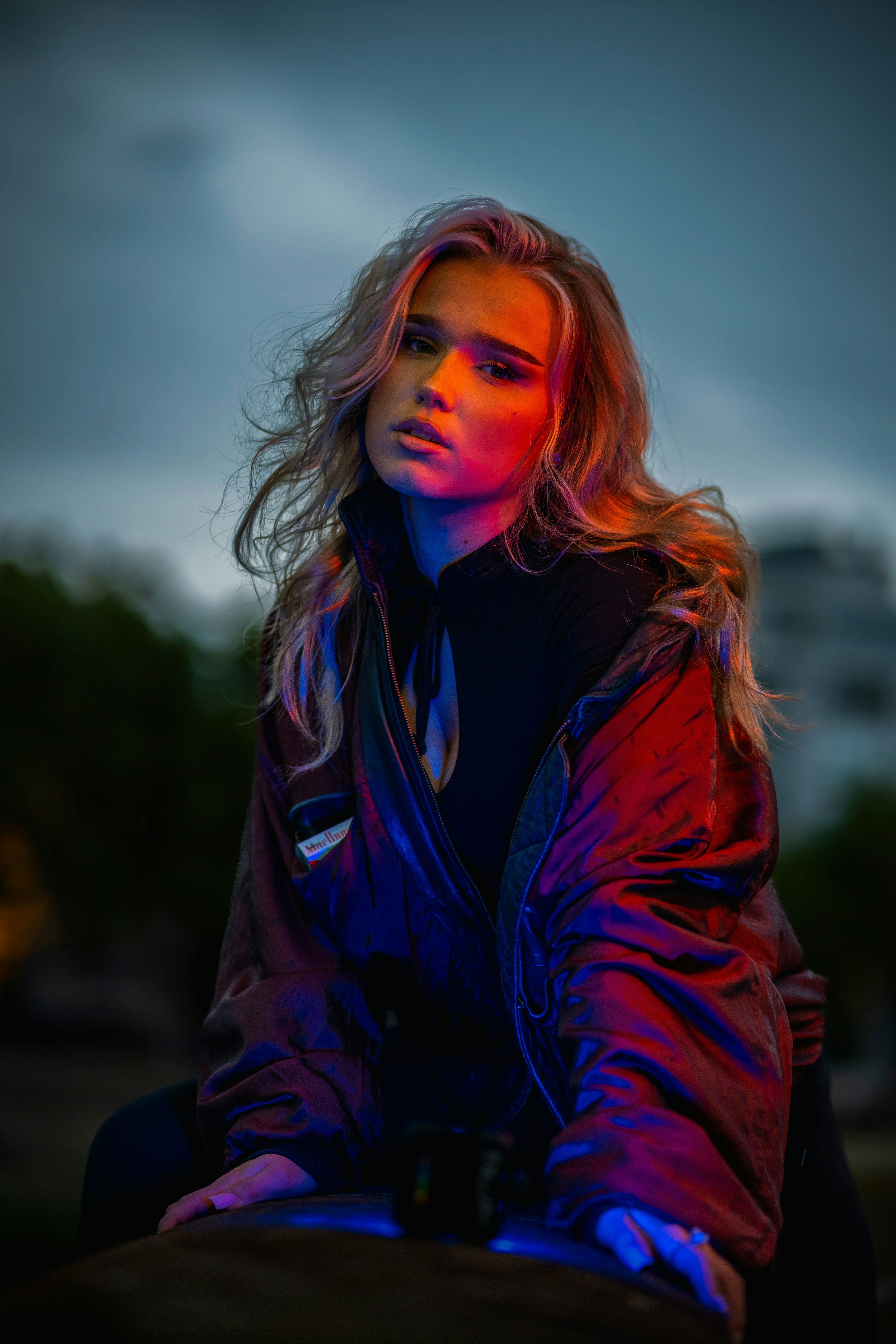 A woman in a black top and dark jacket lit by red and blue light