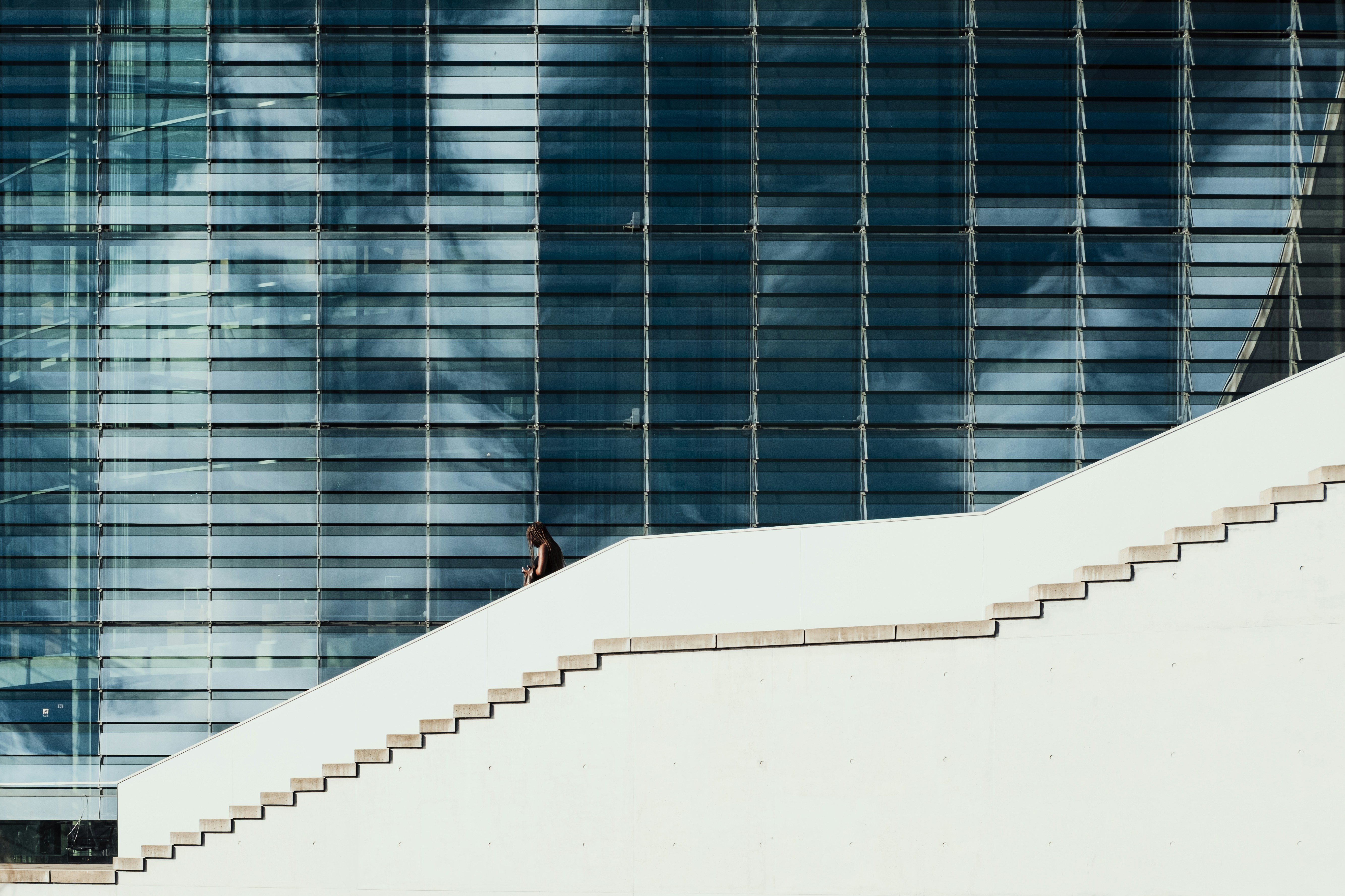 A person walking up white concrete stairs beside a glass building in Berlin
